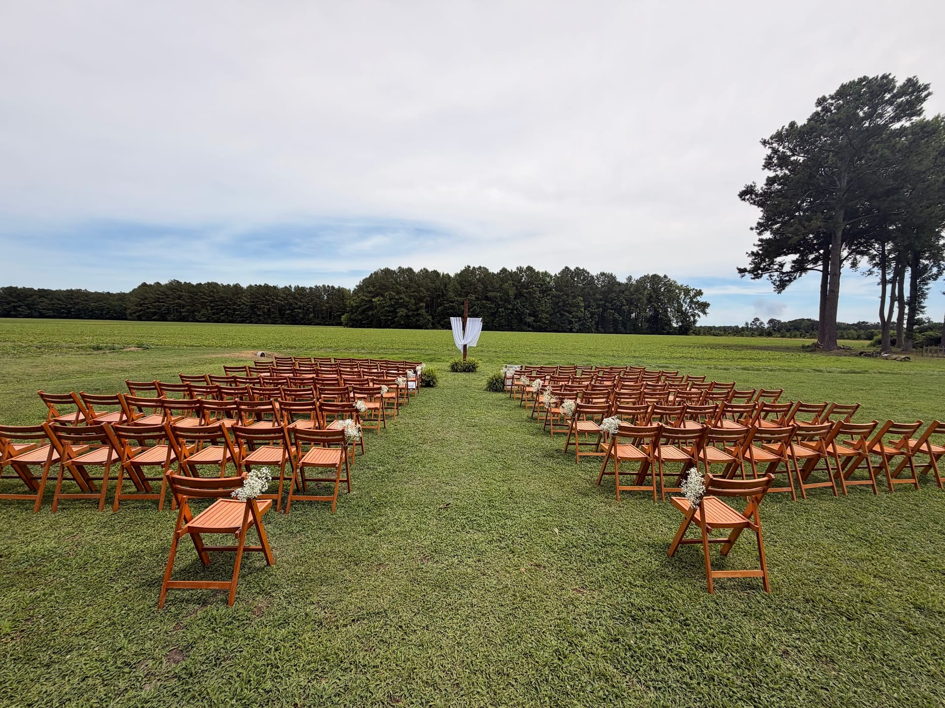Rows of wooden folding chairs arranged on a lush green lawn with white floral aisle markers leading to a draped ceremony arch at Scarborough House outdoor wedding venue.