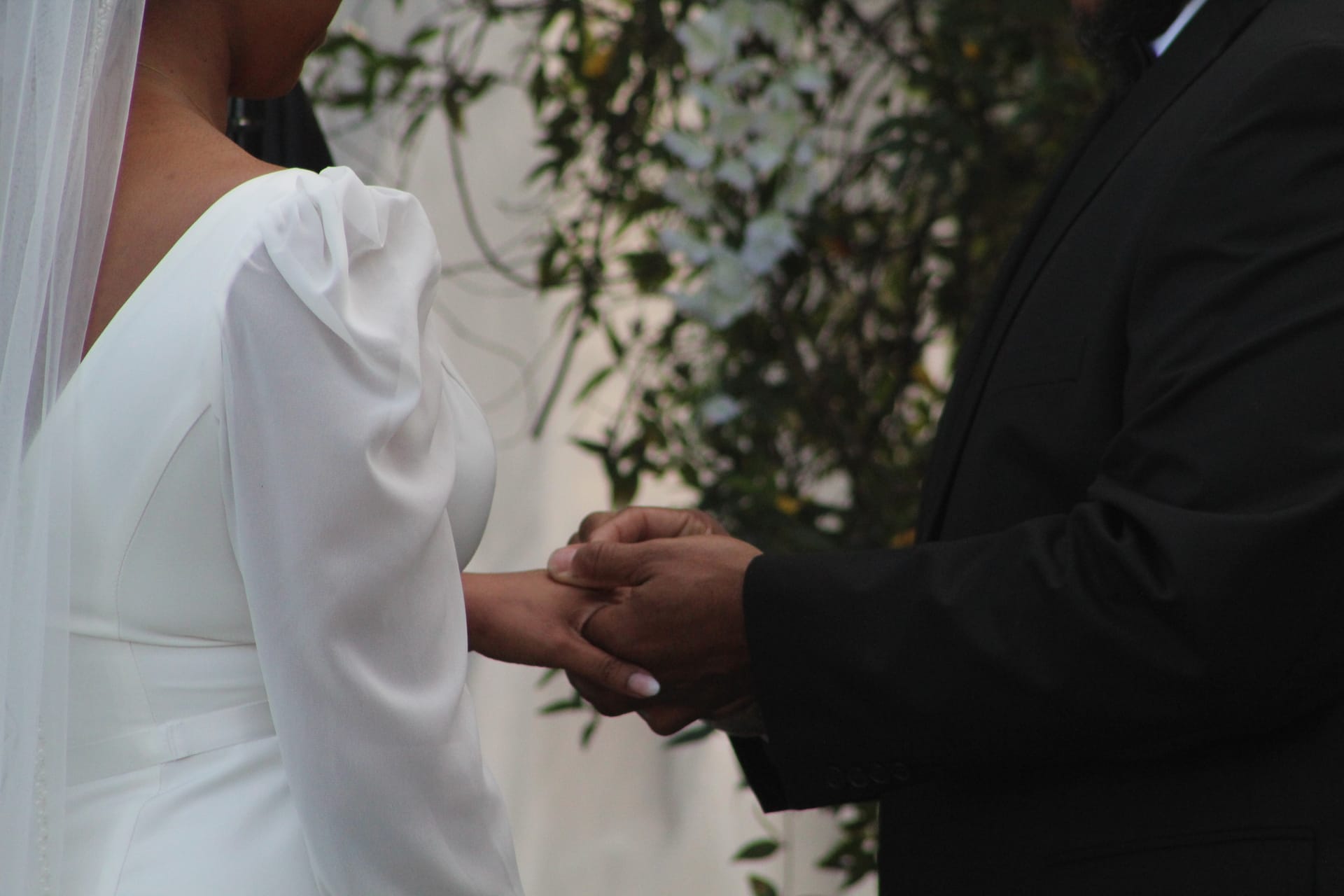 Bride in a white long-sleeve gown and groom in a black suit exchange rings during an outdoor garden wedding ceremony at Scarborough House.
