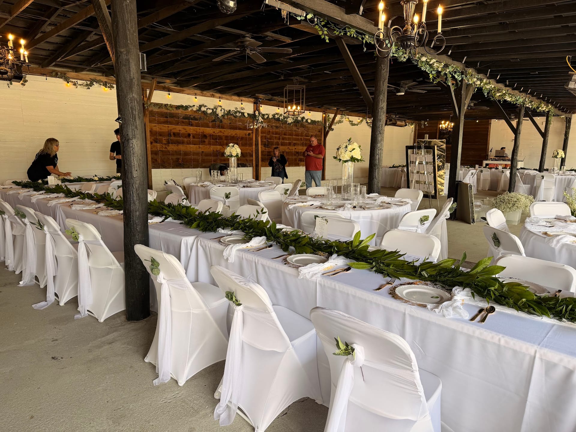 Elegantly set reception tables with white linen chair covers adorned with floral sprigs and lush greenery garland runners inside the grand hall at Scarborough House wedding venue.