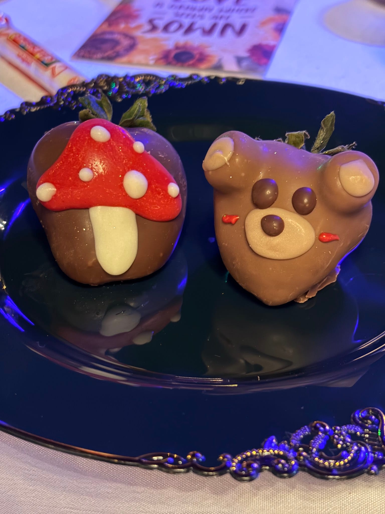 Two chocolate-covered strawberries decorated as a mushroom and a teddy bear displayed on a dark ornate plate at a Scarborough House wedding reception.