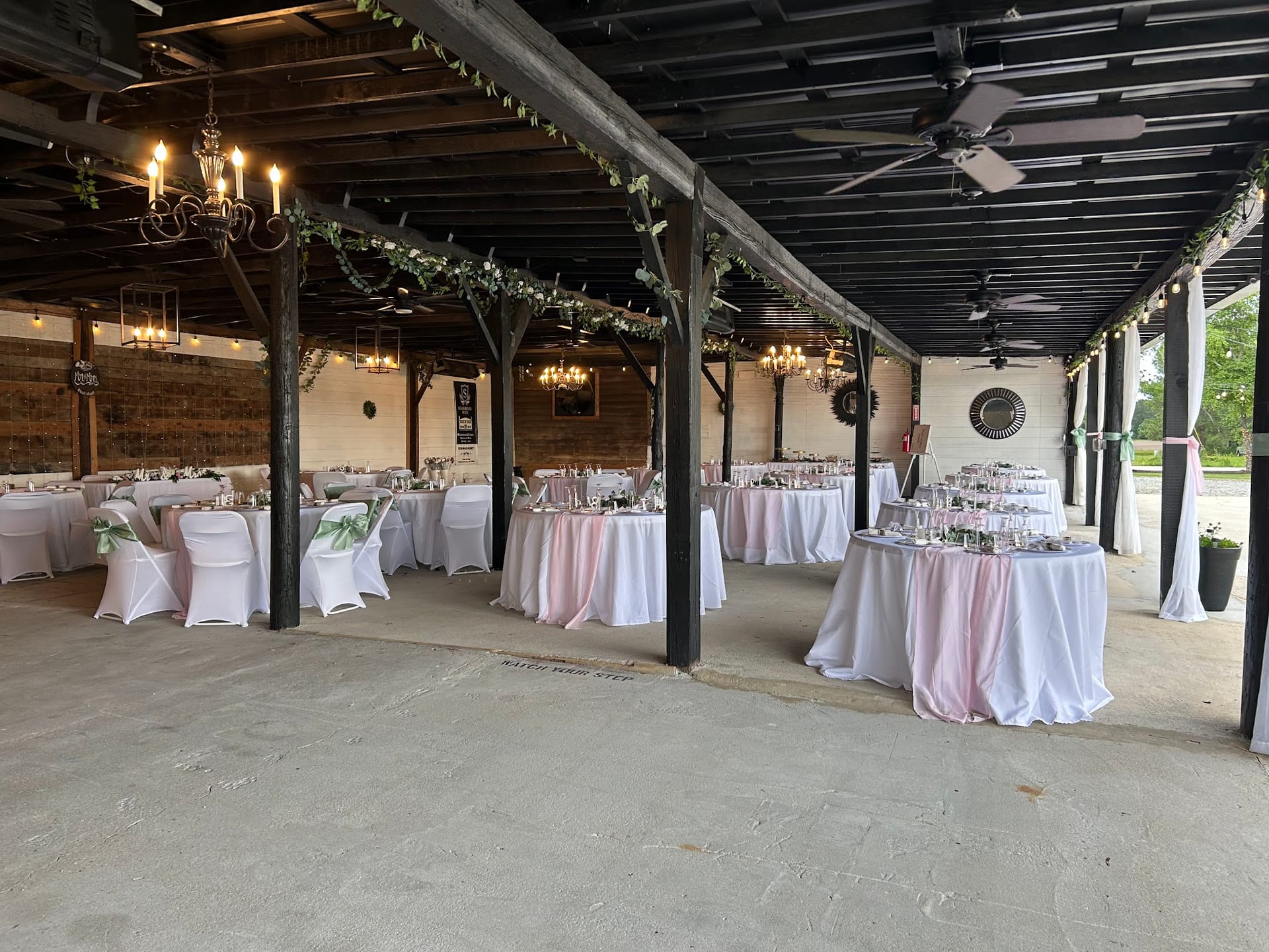 Elegantly decorated open-air pavilion reception space at Scarborough House featuring round tables with blush pink and white linens, greenery garland draped across dark wooden beams, and warm chandelier lighting.