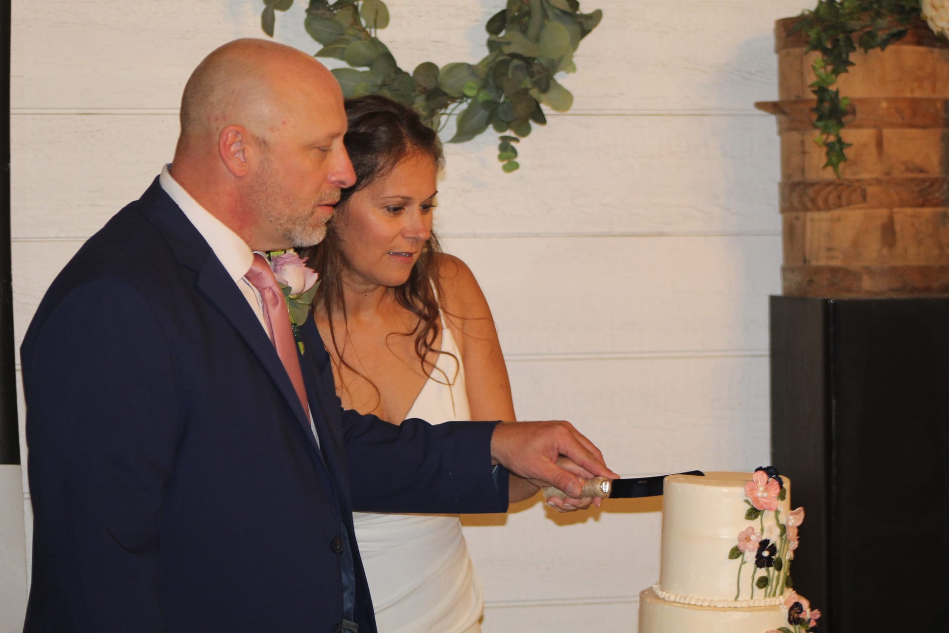 Bride and groom cutting their white floral-decorated wedding cake together in the grand hall at Scarborough House.