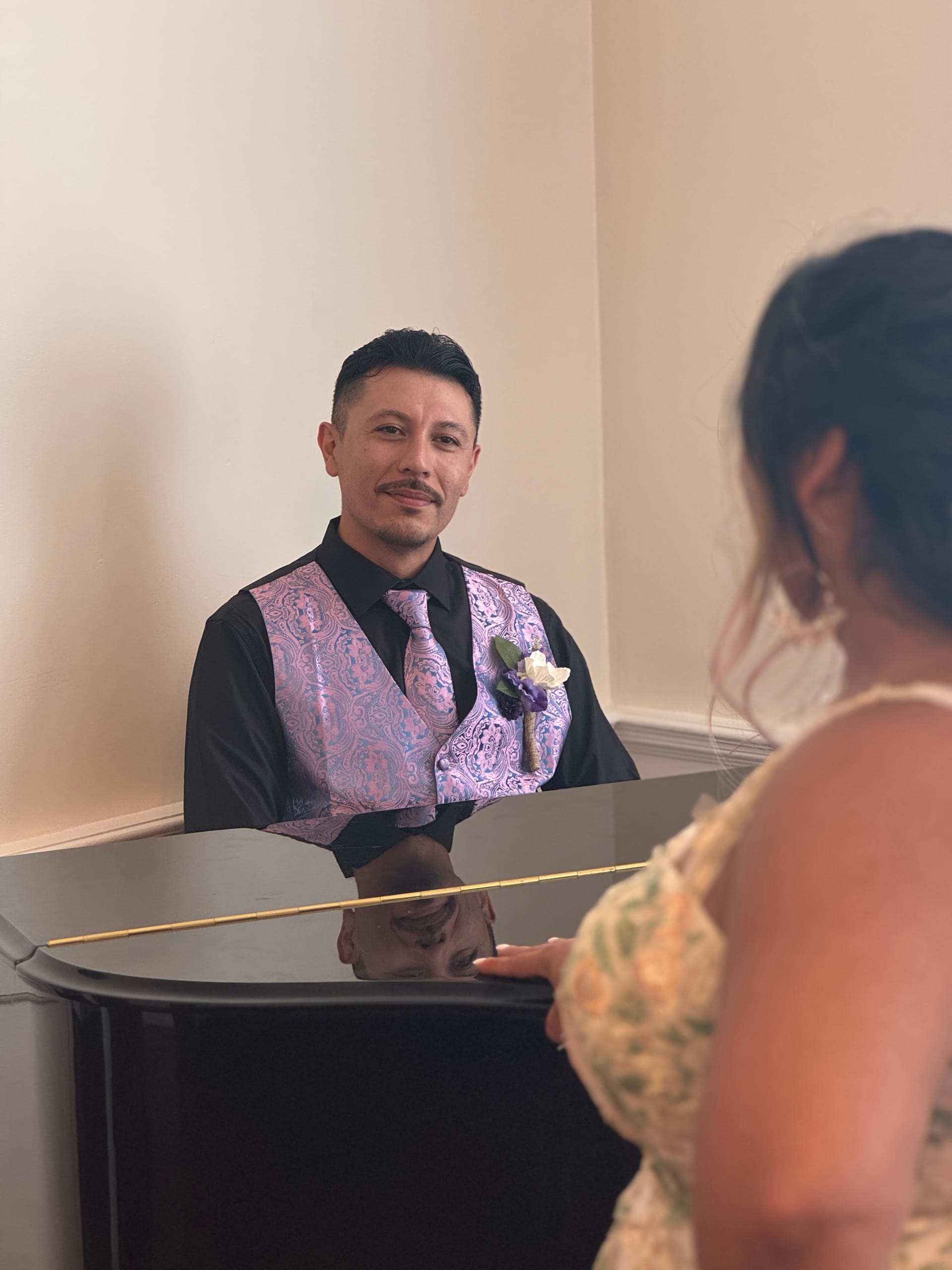 Groom in a lavender paisley vest and boutonniere smiles warmly at his bride during an indoor wedding ceremony at Scarborough House.