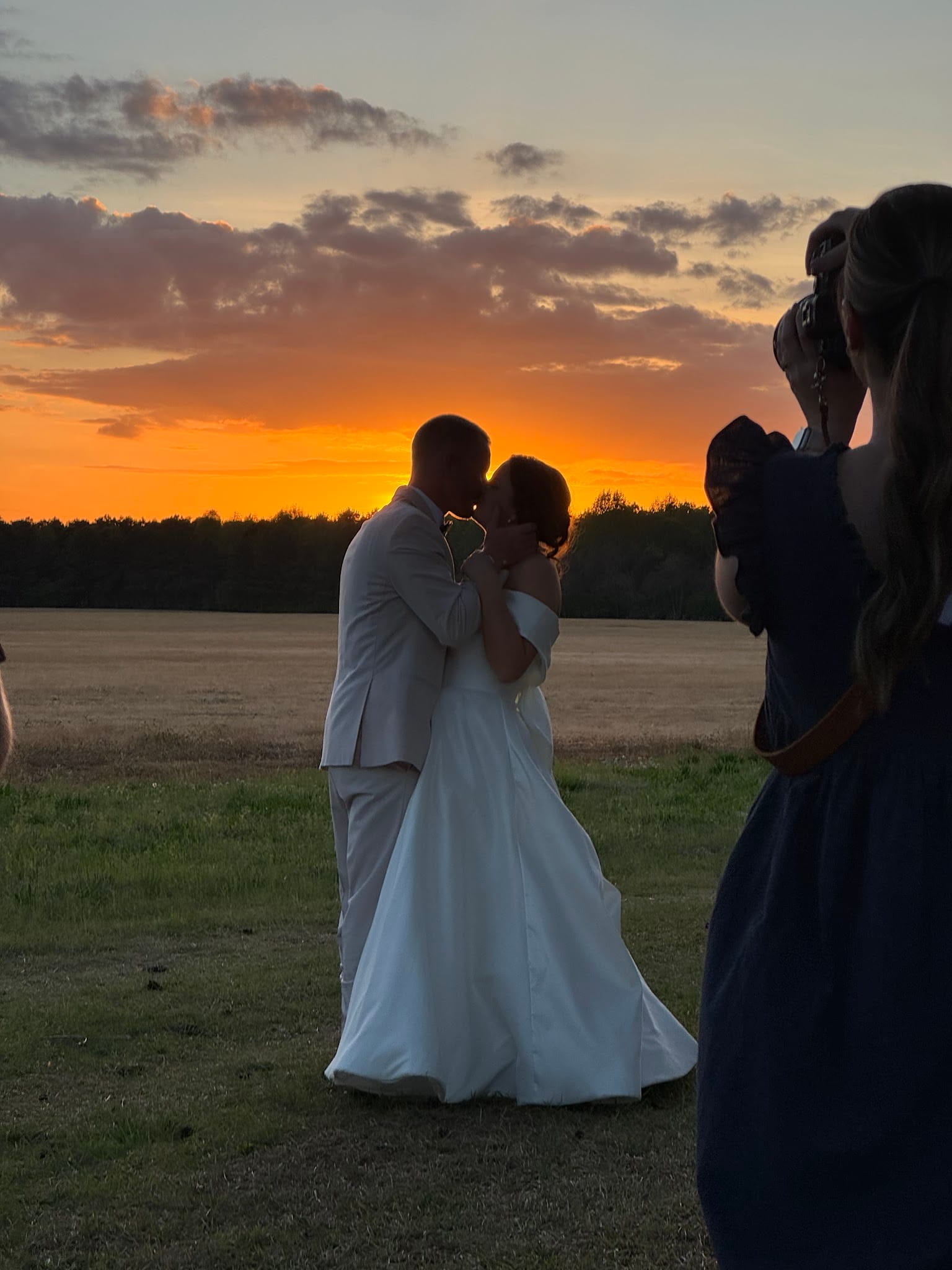 Bride and groom share a kiss in silhouette against a brilliant orange and gold sunset over open farmland fields at Scarborough House estate wedding venue.
