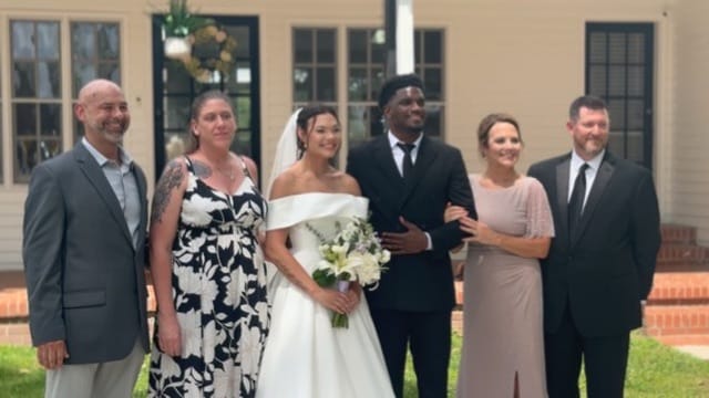 Bride in off-shoulder gown and groom in black suit pose with four family members in front of the historic 1821 Scarborough House manor on their wedding day.