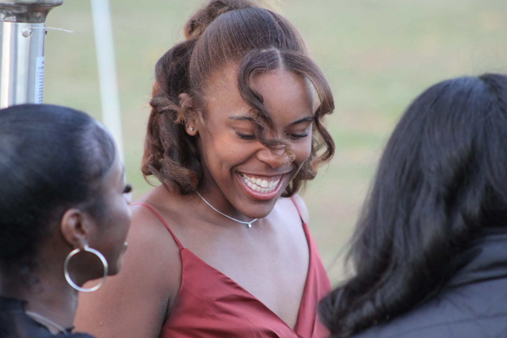 A joyful young woman in a rose-colored gown laughs warmly while socializing with guests at an outdoor evening reception.
