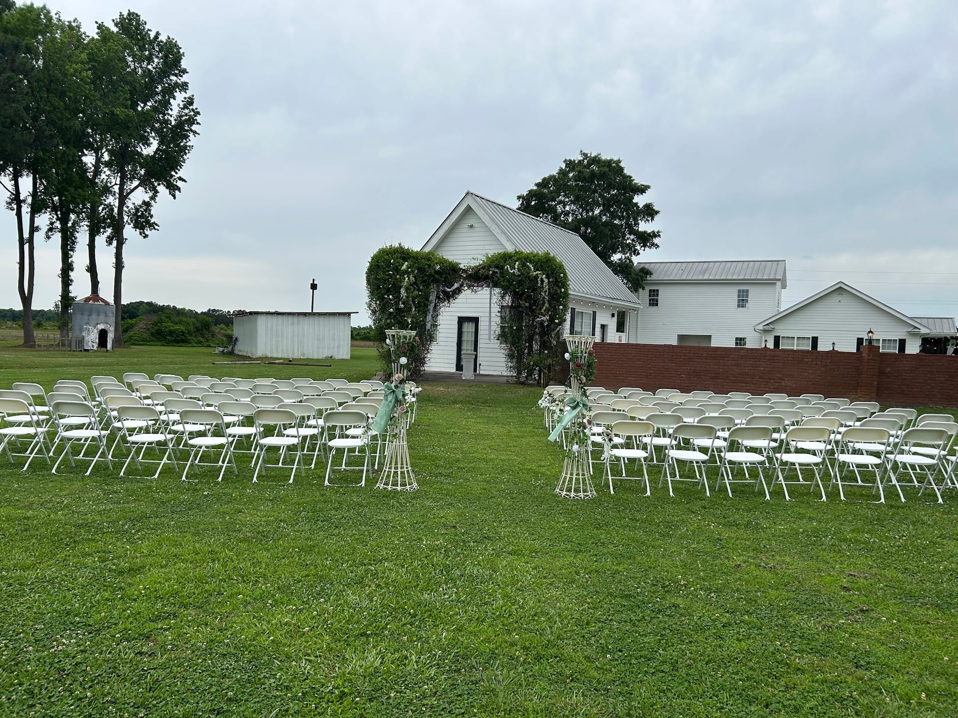 Rows of white folding chairs arranged on a green lawn facing a floral arch at Scarborough House outdoor wedding ceremony venue under an overcast sky.