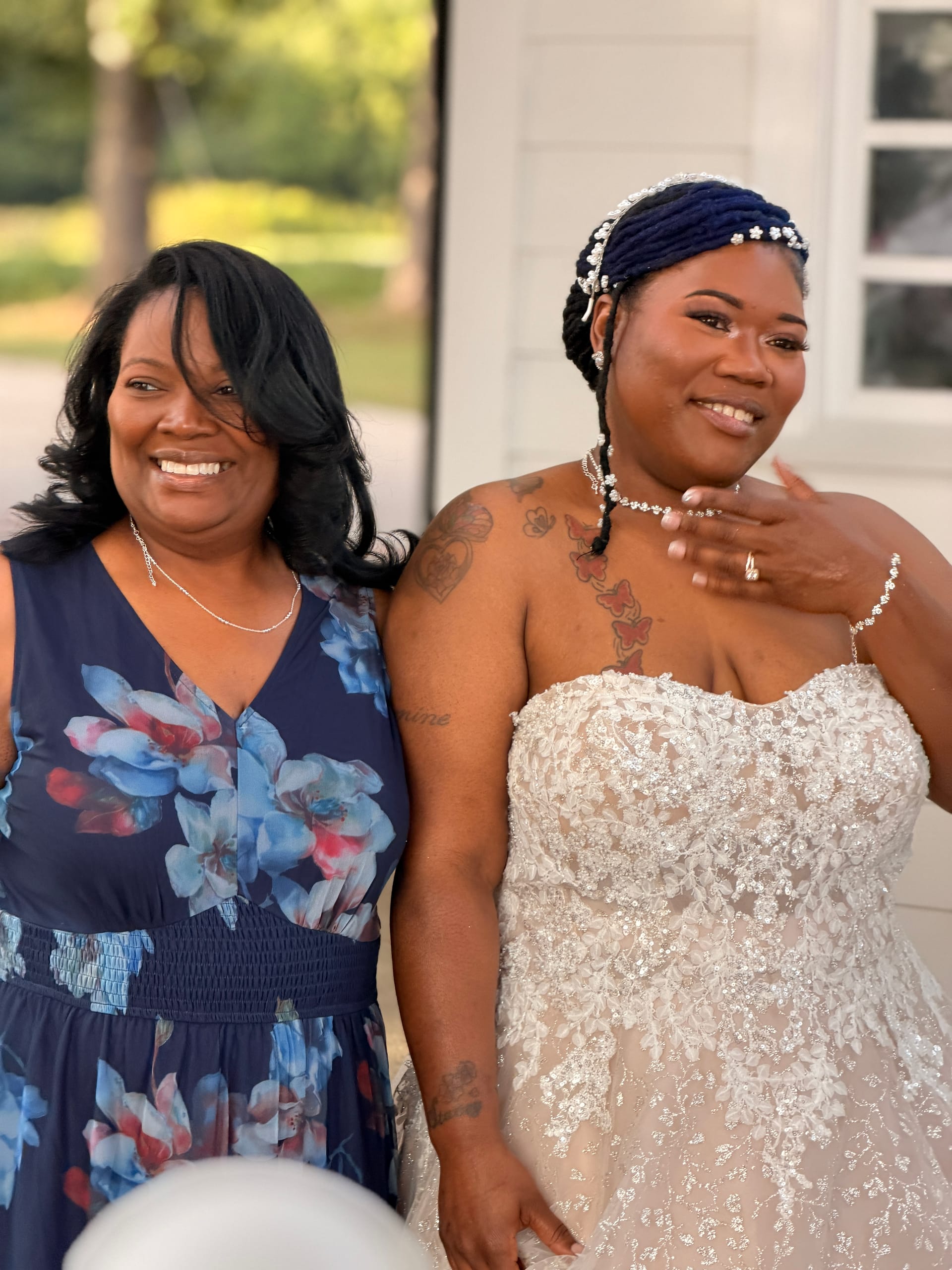 A smiling bride in a strapless beaded gown poses with a female guest in a navy floral dress outside the historic Scarborough House estate.