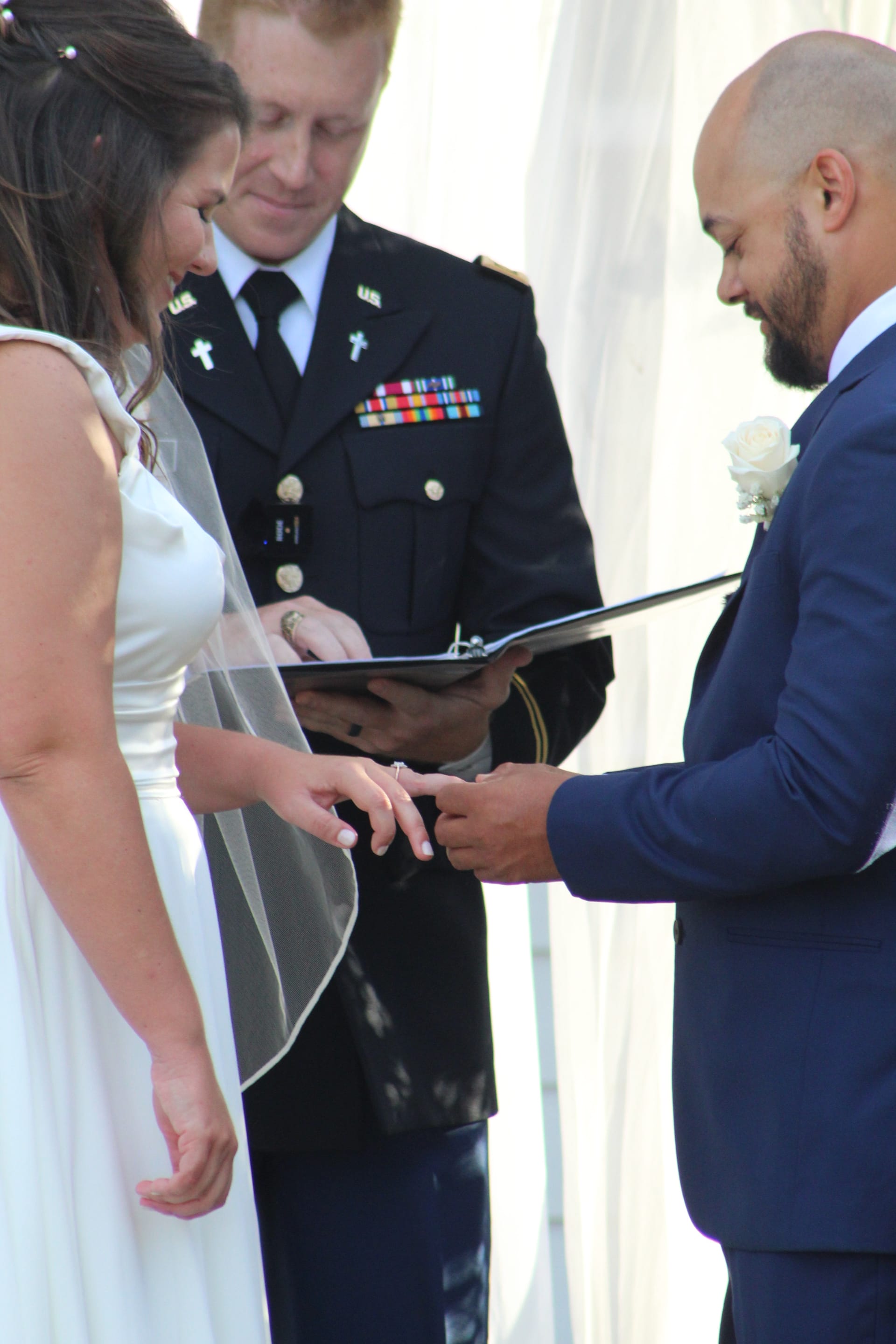 Groom placing a wedding ring on his brides finger during an outdoor ceremony officiated by a uniformed military chaplain at Scarborough House.