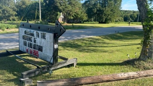 A marquee arrow sign reading Welcome to the Wedding of Uri and Arturo with a date in 2025 placed on the lawn entrance of Scarborough House historic wedding venue surrounded by oak trees and green grass.