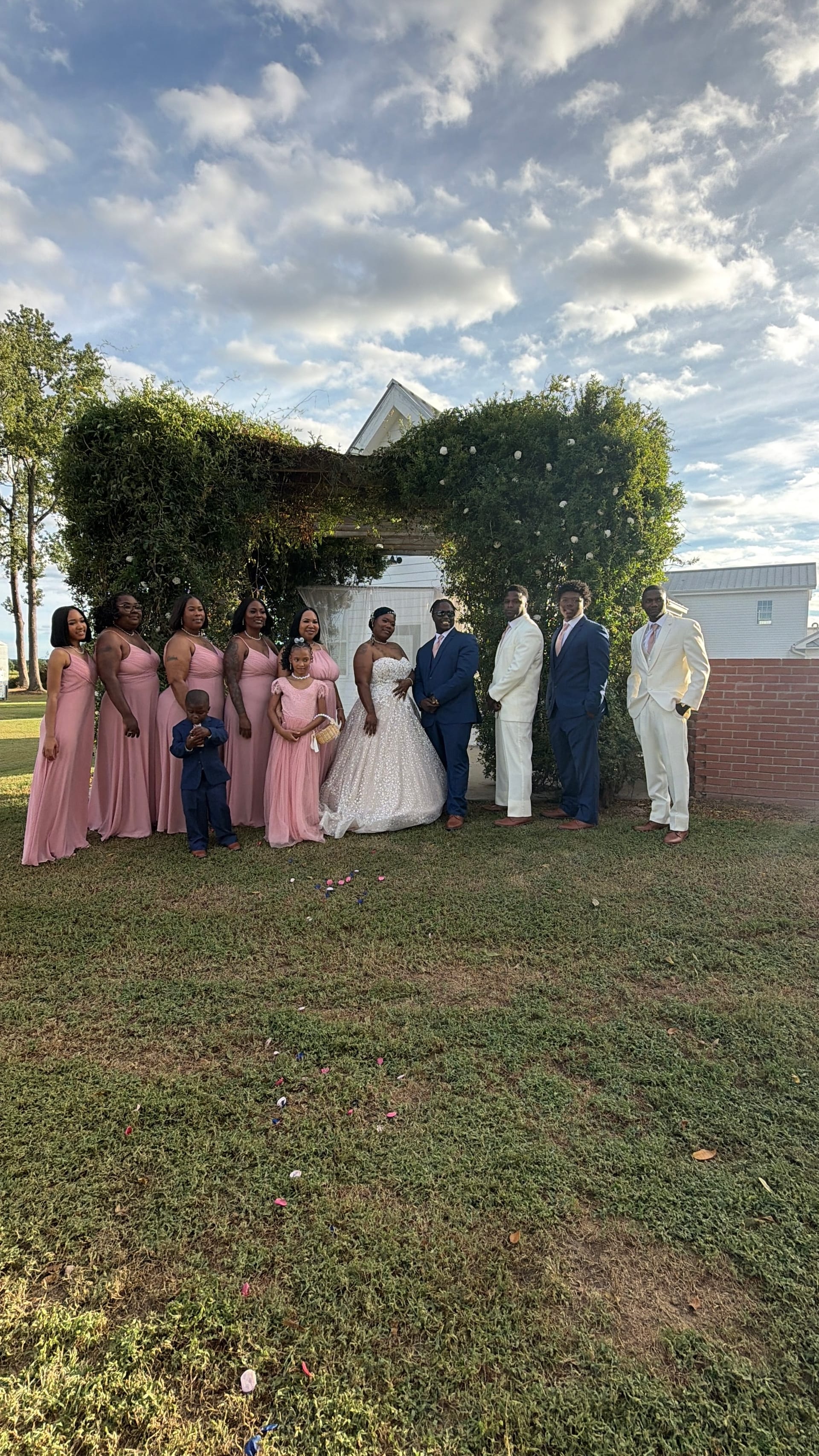 Wedding party in pink bridesmaid gowns and navy suits pose with the bride in a white ballgown and groom before an ivy-covered chapel on the ceremony lawn at Scarborough House.