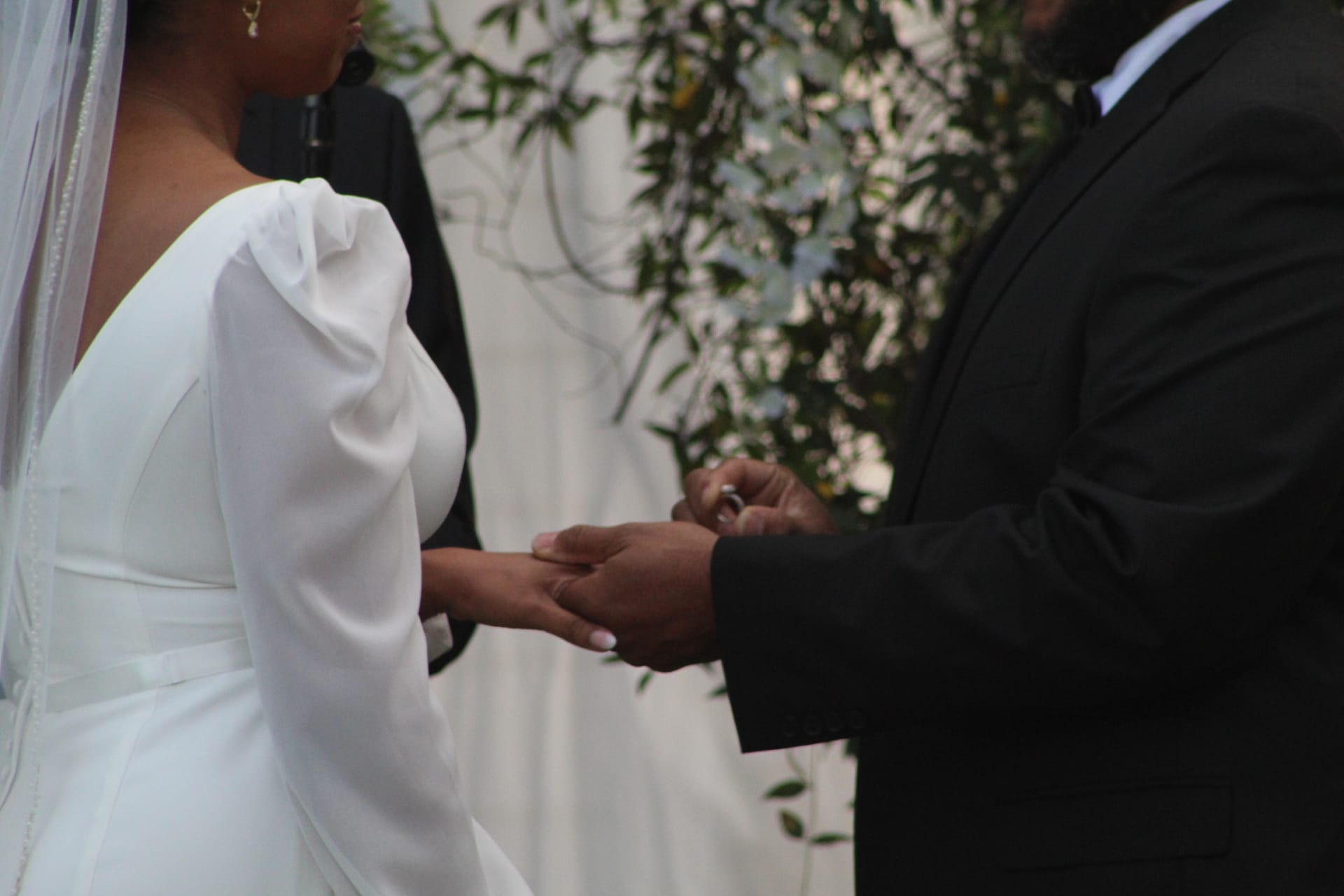 Groom placing a wedding ring on the bride's finger during the outdoor ceremony at Scarborough House, with lush greenery softly blurred in the background.