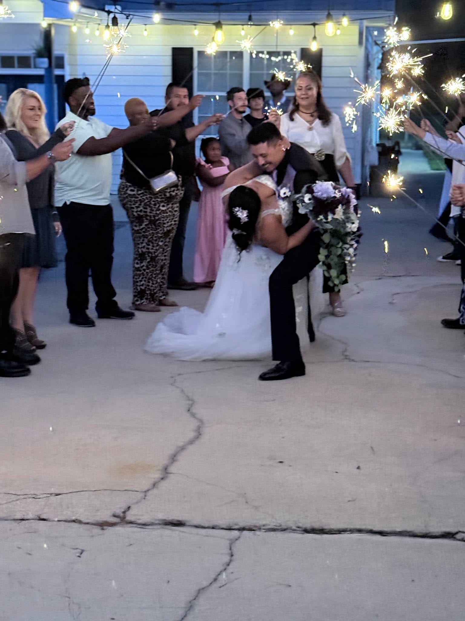 Groom dips and kisses bride in a white gown while wedding guests line a sparkler-lit exit tunnel outside the historic Scarborough House venue at night.