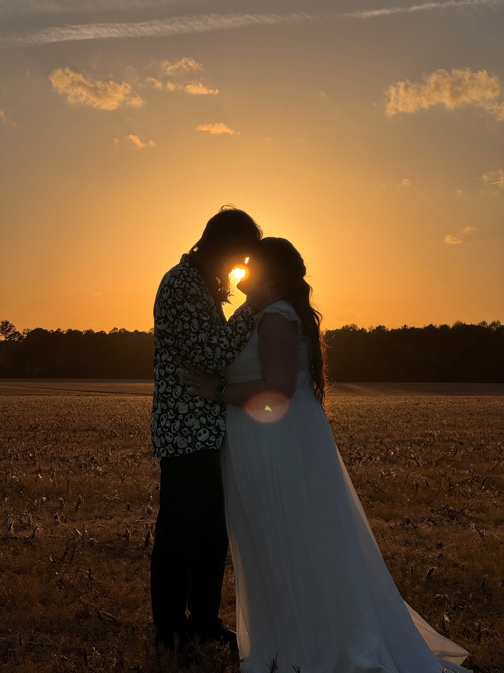 Bride and groom silhouetted against a glowing golden sunset over open farmland fields at Scarborough House with a dramatic lens flare between them.