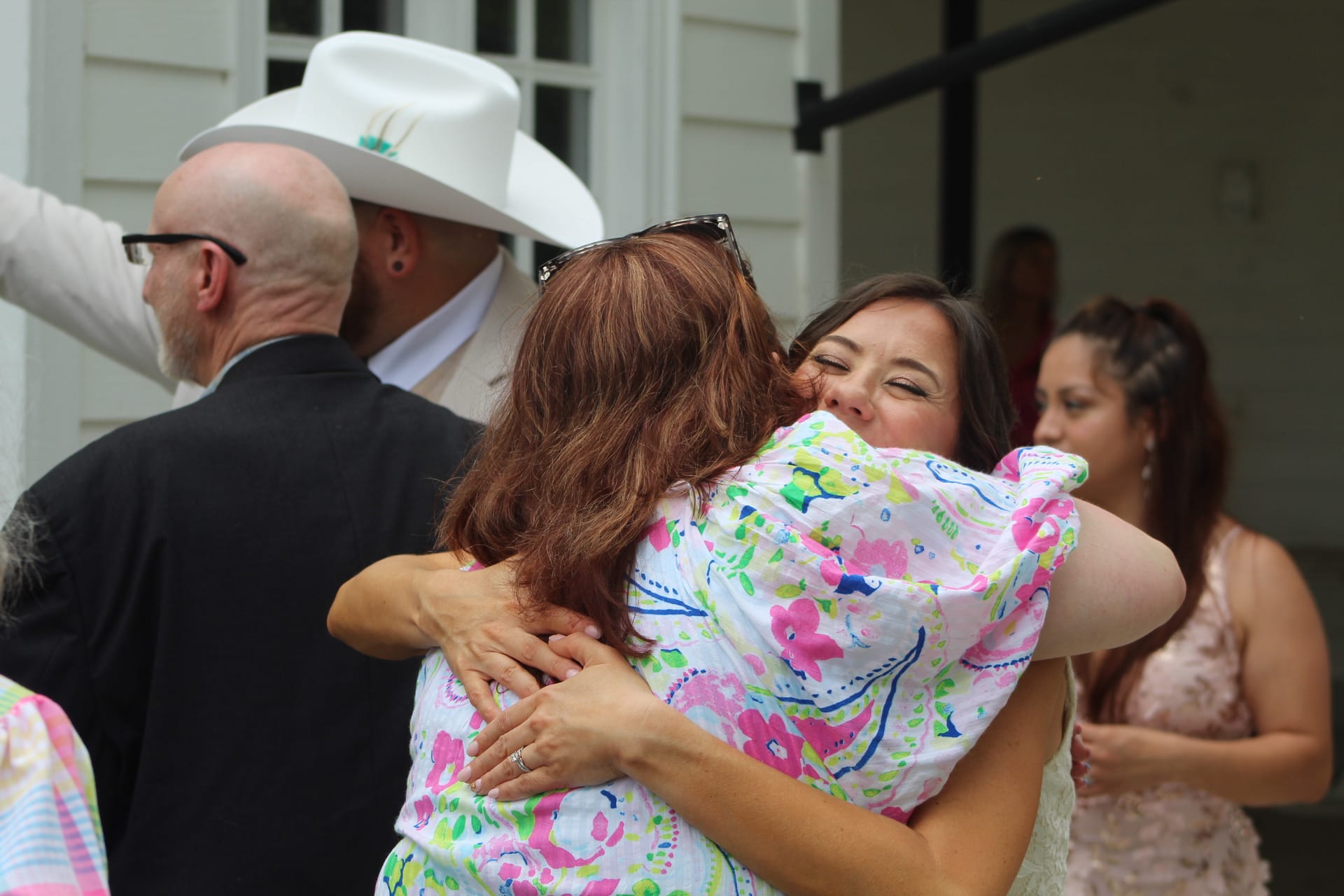 Two women share a warm embrace outside the historic Scarborough House estate during a wedding celebration.