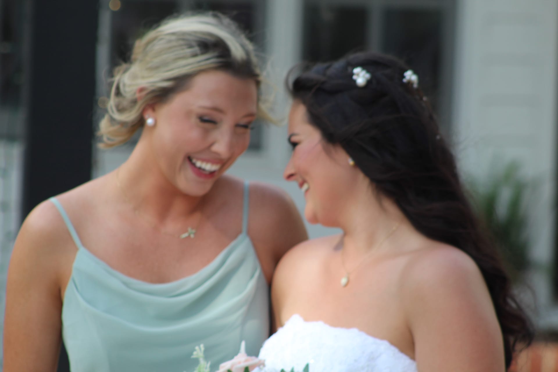Bride in white gown and bridesmaid in sage green dress laughing together joyfully outdoors at Scarborough House historic estate wedding venue.