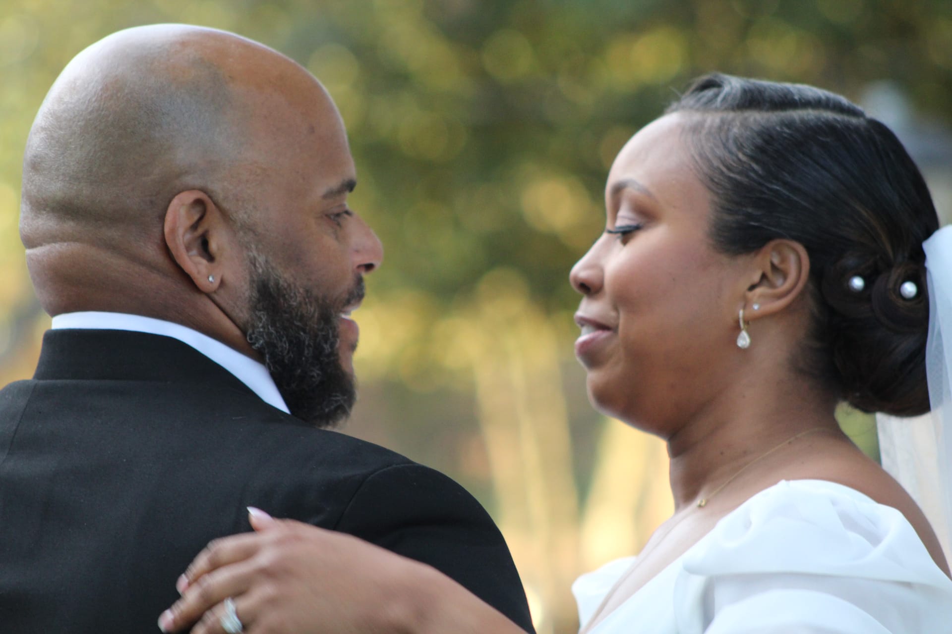 Bride in a white off-shoulder gown gazes tenderly at her tuxedo-clad groom during an intimate outdoor moment at Scarborough House estate.