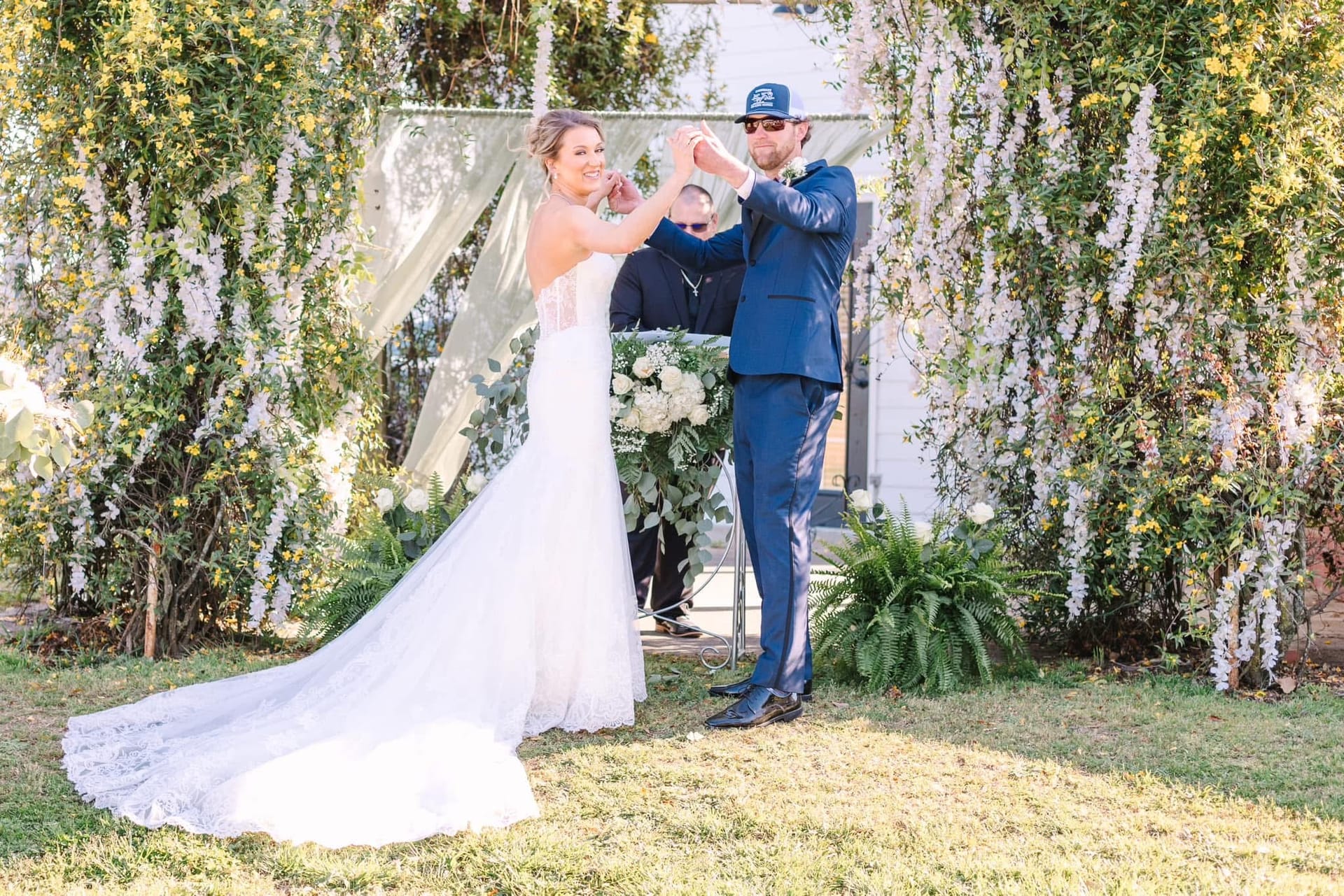 Bride and groom share a celebratory spin beneath a lush floral and greenery arch on the ceremony lawn at Scarborough House historic estate wedding venue.
