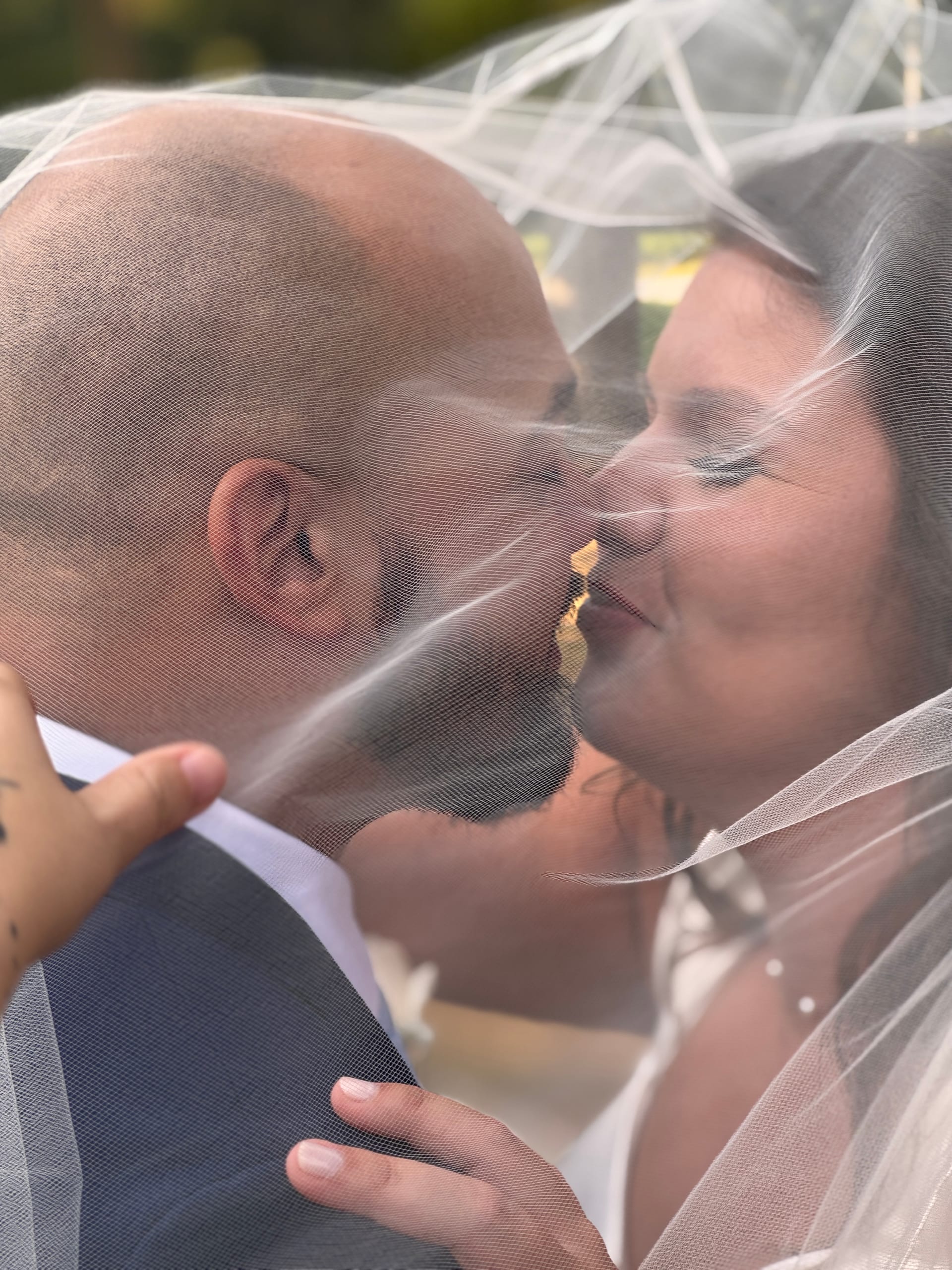 Bride and groom share a first kiss beneath a flowing bridal veil at an outdoor wedding ceremony at Scarborough House estate.