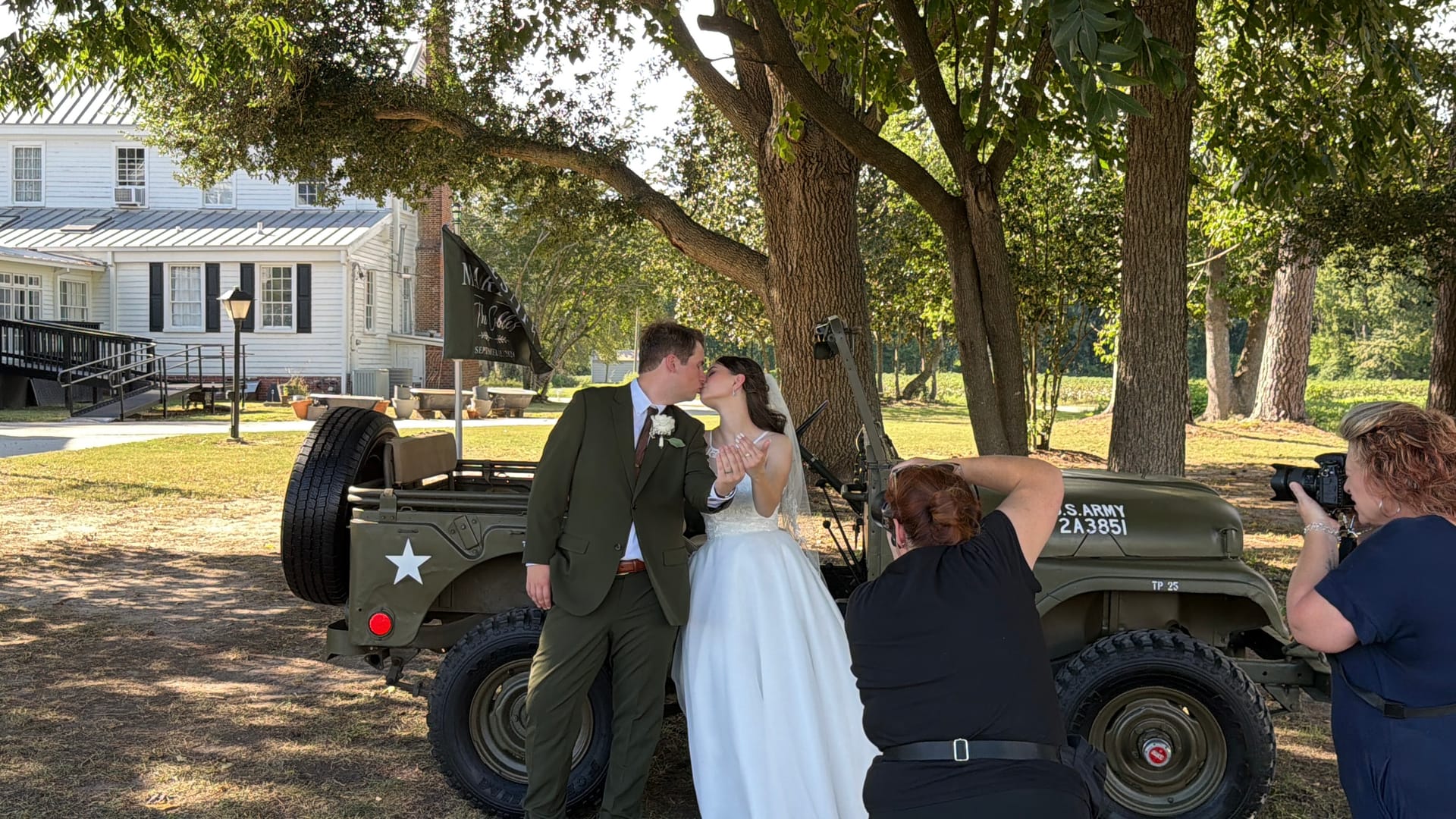 Bride and groom share a kiss in front of a vintage U.S. Army Jeep beneath sweeping oak trees on the historic grounds of Scarborough House estate wedding venue.