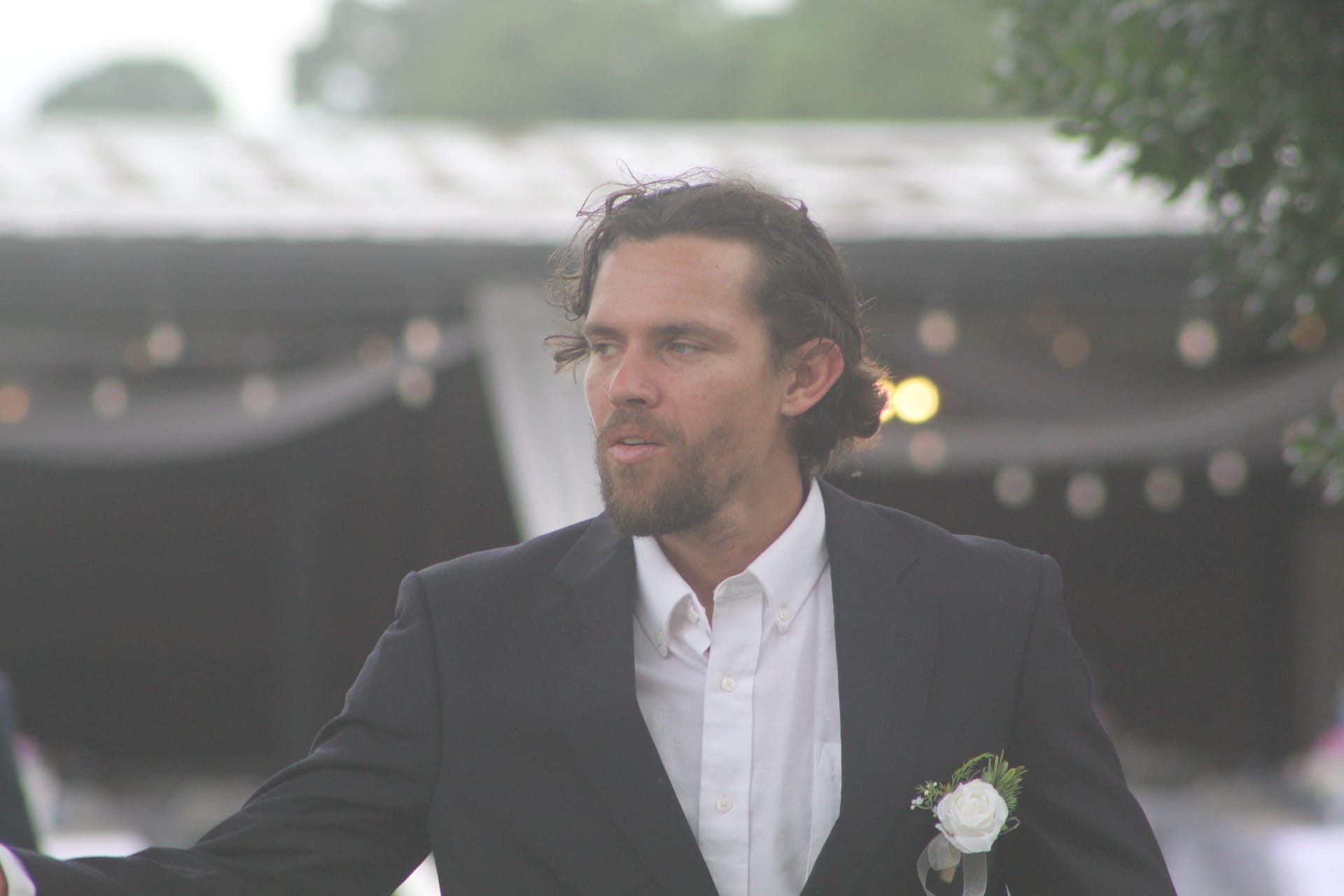Groom in a black suit with white rose boutonniere gazes thoughtfully to the side beneath a softly lit reception tent at Scarborough House.