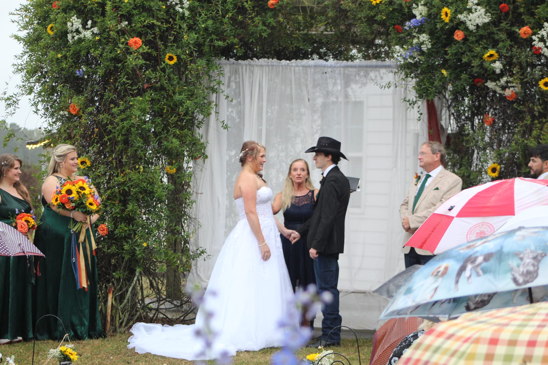 Bride and groom exchange vows beneath a lush floral arch decorated with sunflowers and colorful blooms at Scarborough House historic estate wedding venue.