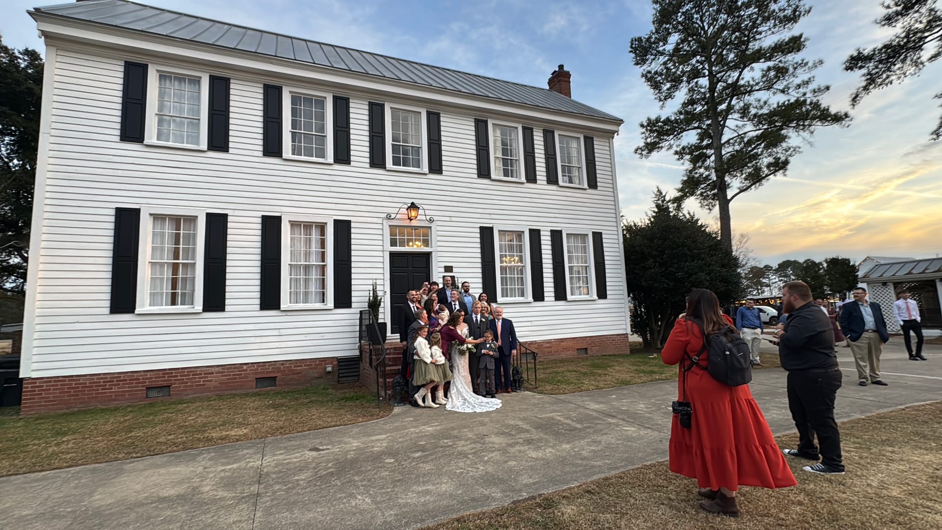 Wedding party group portrait posed on the front steps of the 1821 Scarborough House manor at dusk with photographers capturing the moment in the foreground.