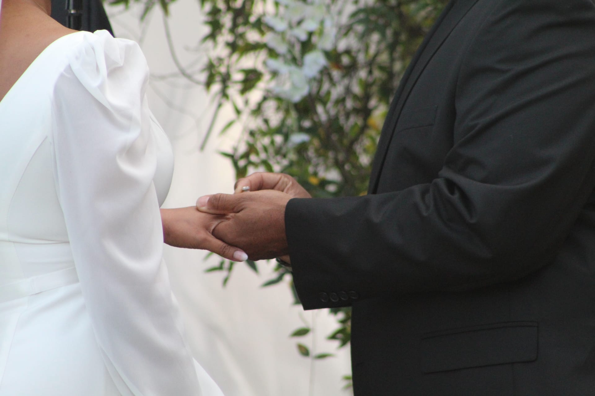Groom in a black suit placing a wedding ring on the brides finger during the outdoor ceremony at Scarborough House historic estate.