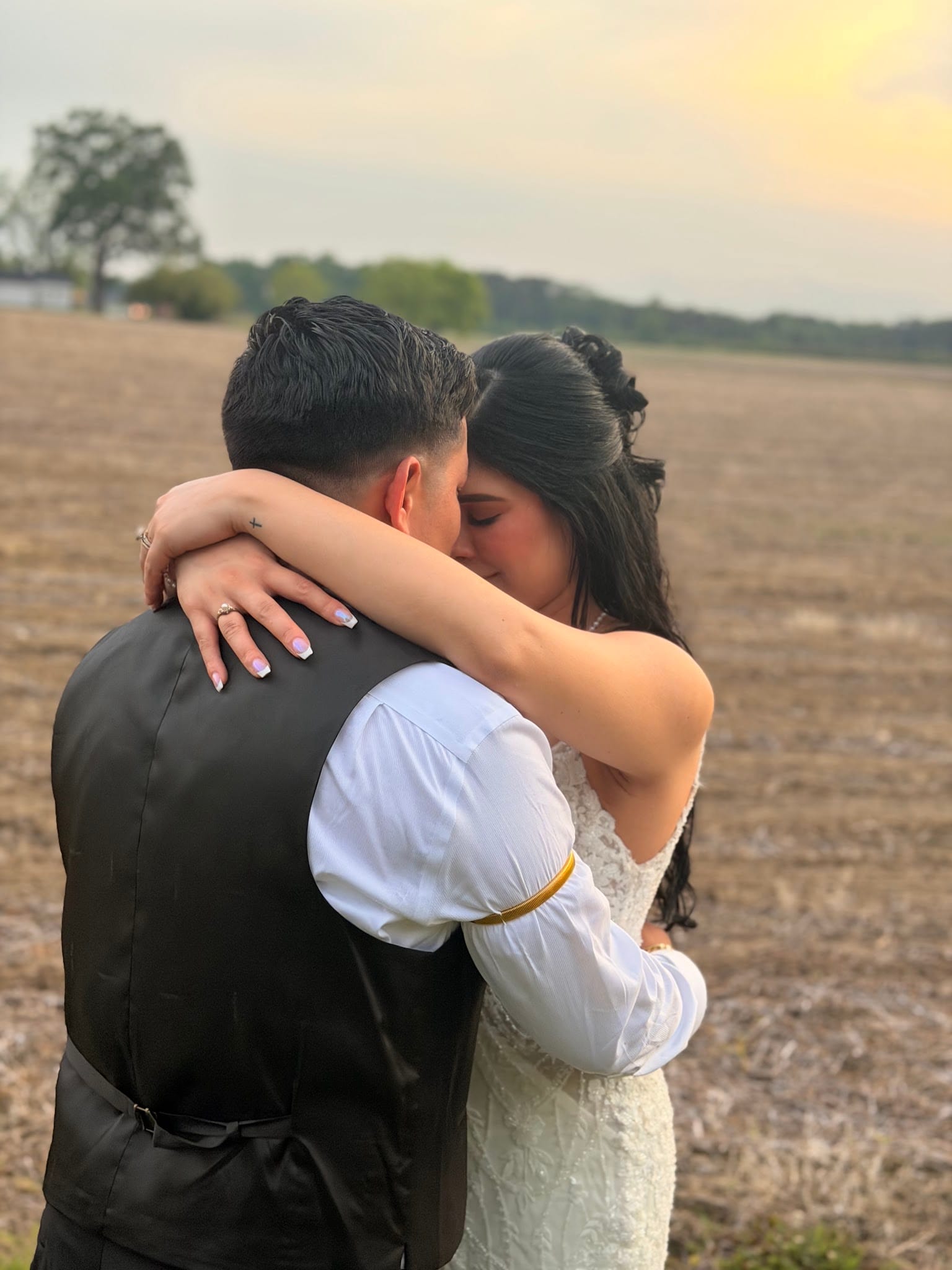 Bride and groom share a romantic kiss at sunset in the open farmland fields at Scarborough House, with warm golden light glowing across the horizon behind them.
