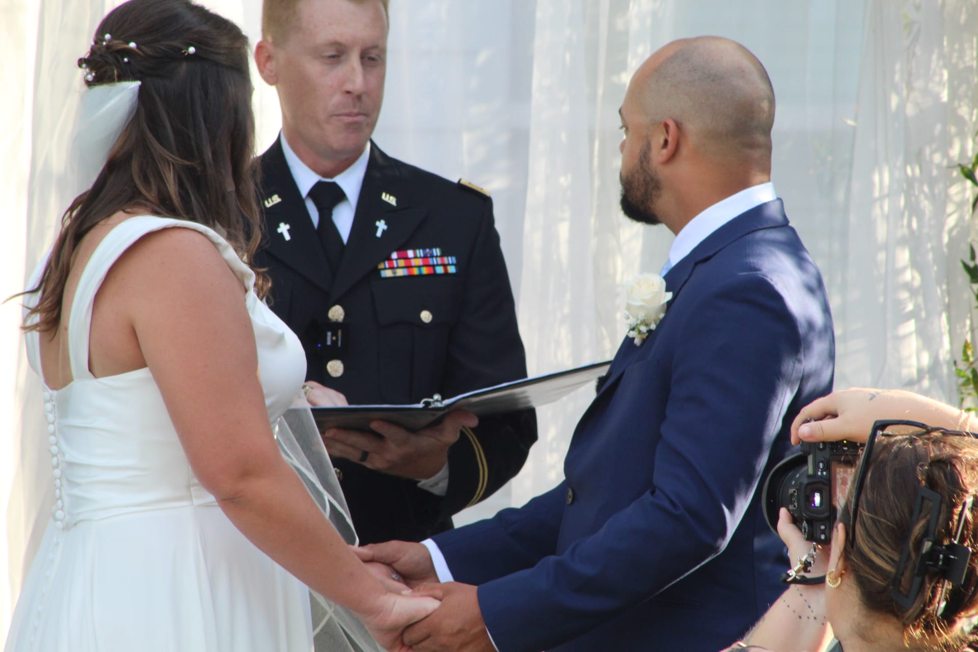 Bride and groom hold hands during their outdoor wedding ceremony officiated by a military officer in dress uniform at Scarborough House estate.