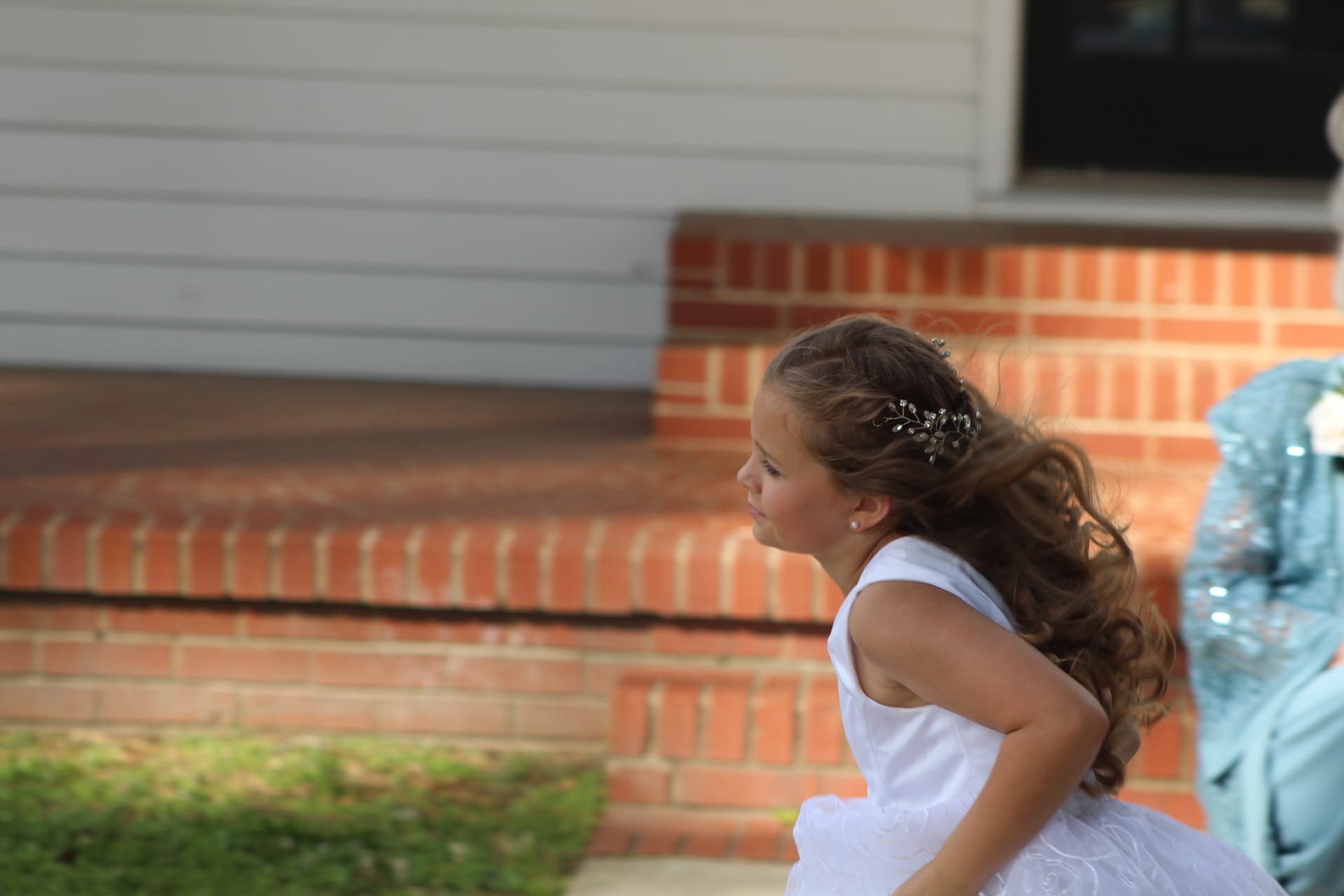 A young flower girl in a white dress running near the brick front steps of a historic estate wedding venue.