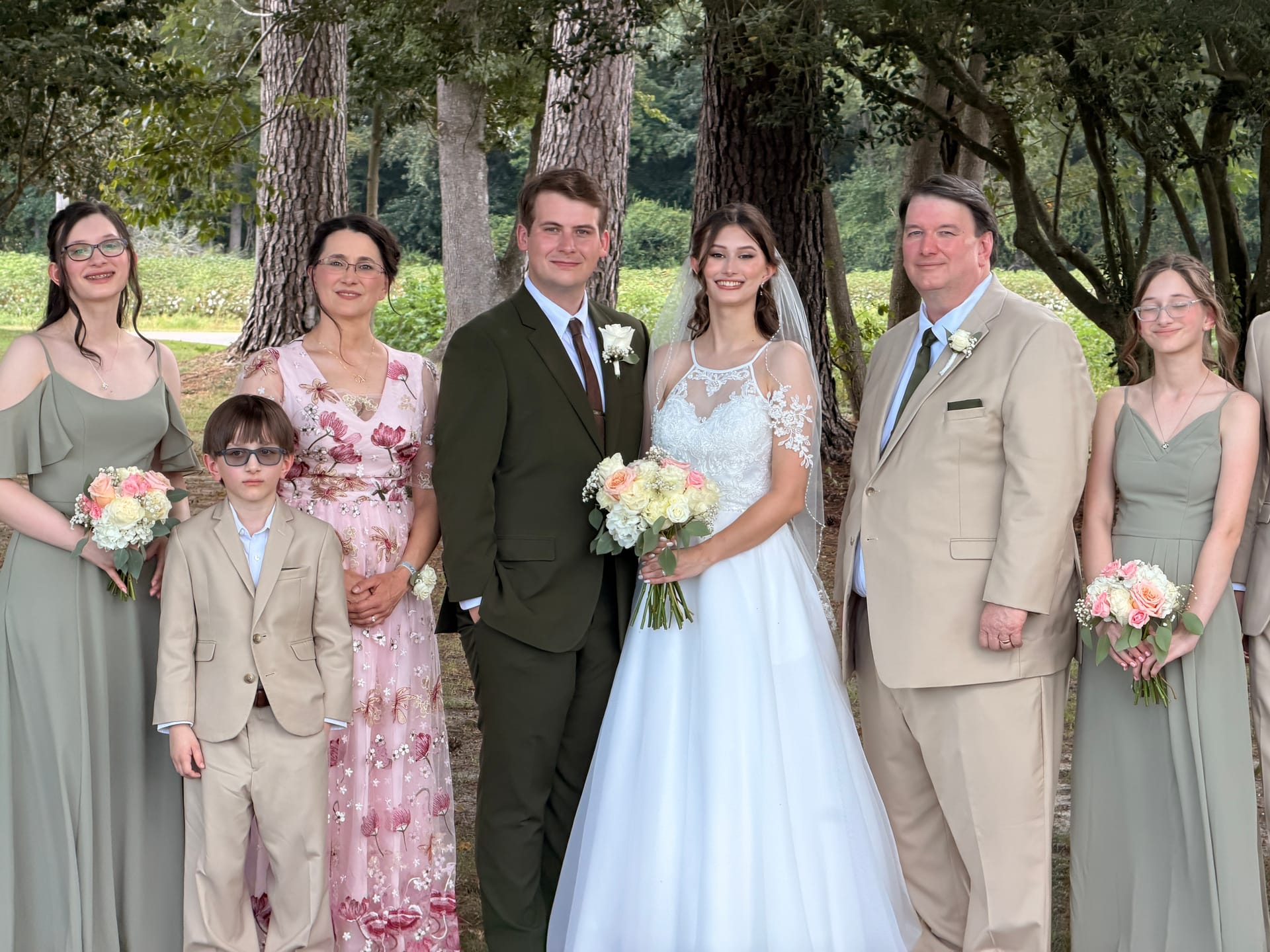 Bride and groom pose with family members including bridesmaids and parents beneath towering oak trees at Scarborough House wedding venue.