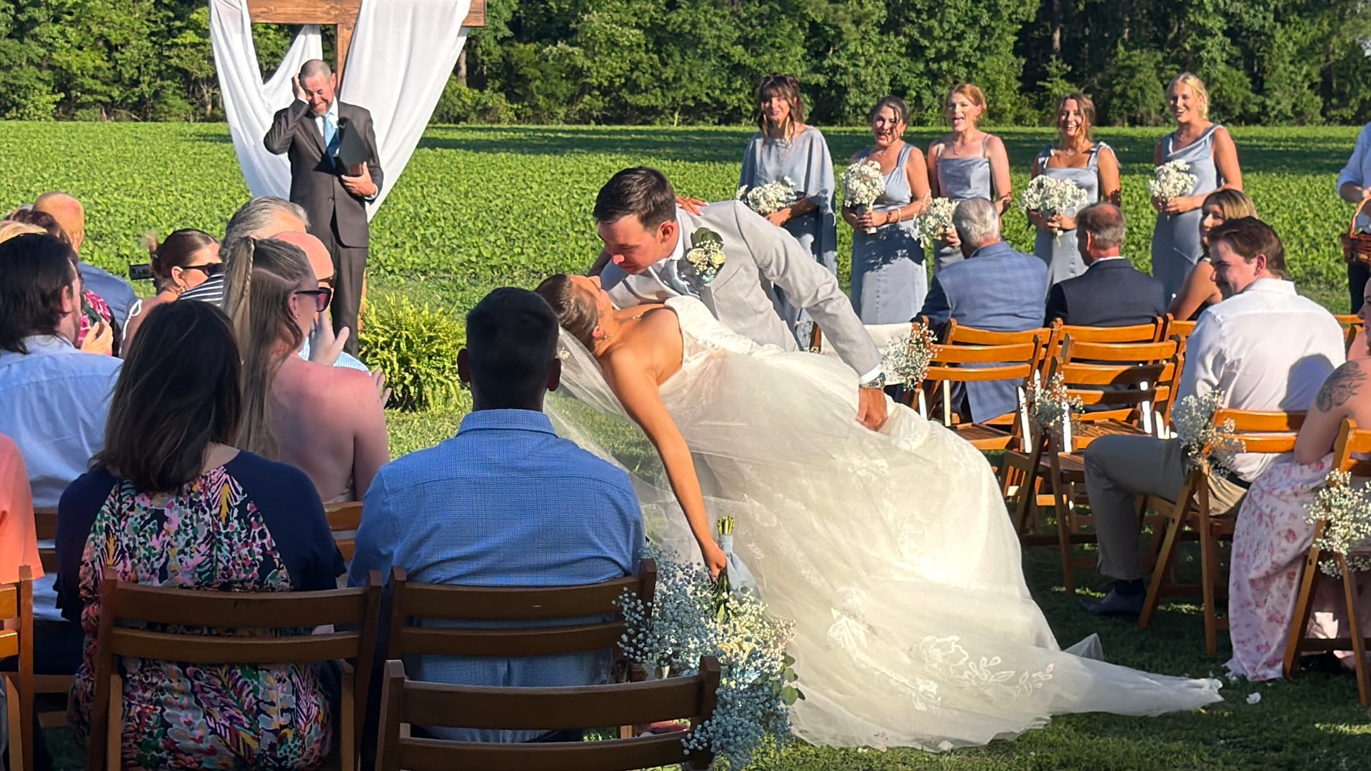 Groom dips bride for a kiss during their wedding recessional on the ceremony lawn at Scarborough House with bridesmaids and guests cheering in golden afternoon light.
