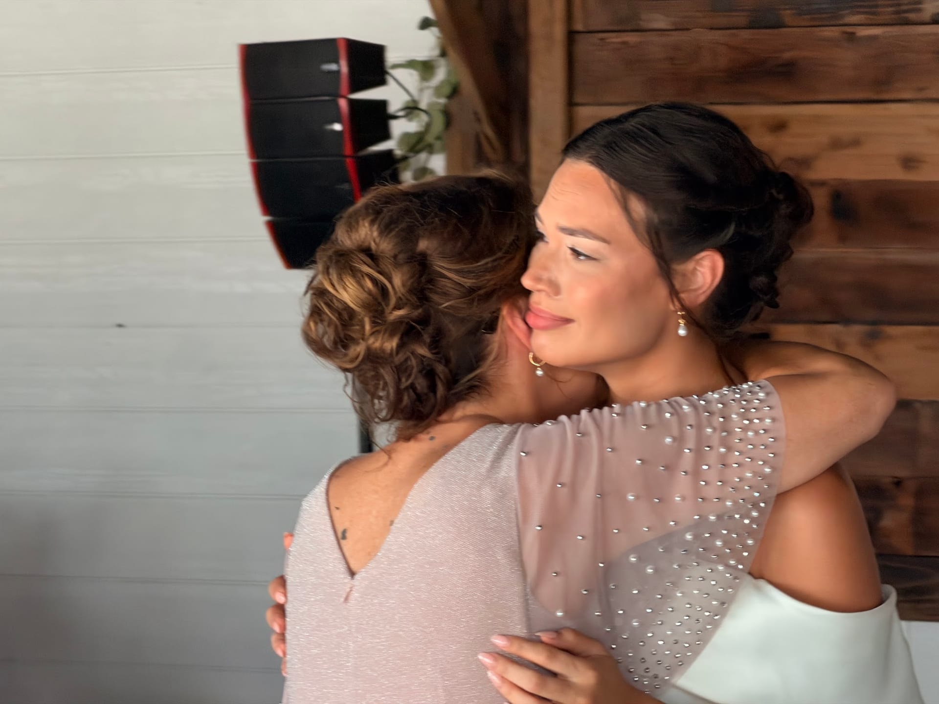Bride in a beaded gown shares a heartfelt embrace with a guest in front of a rustic wood-paneled wall at Scarborough House.