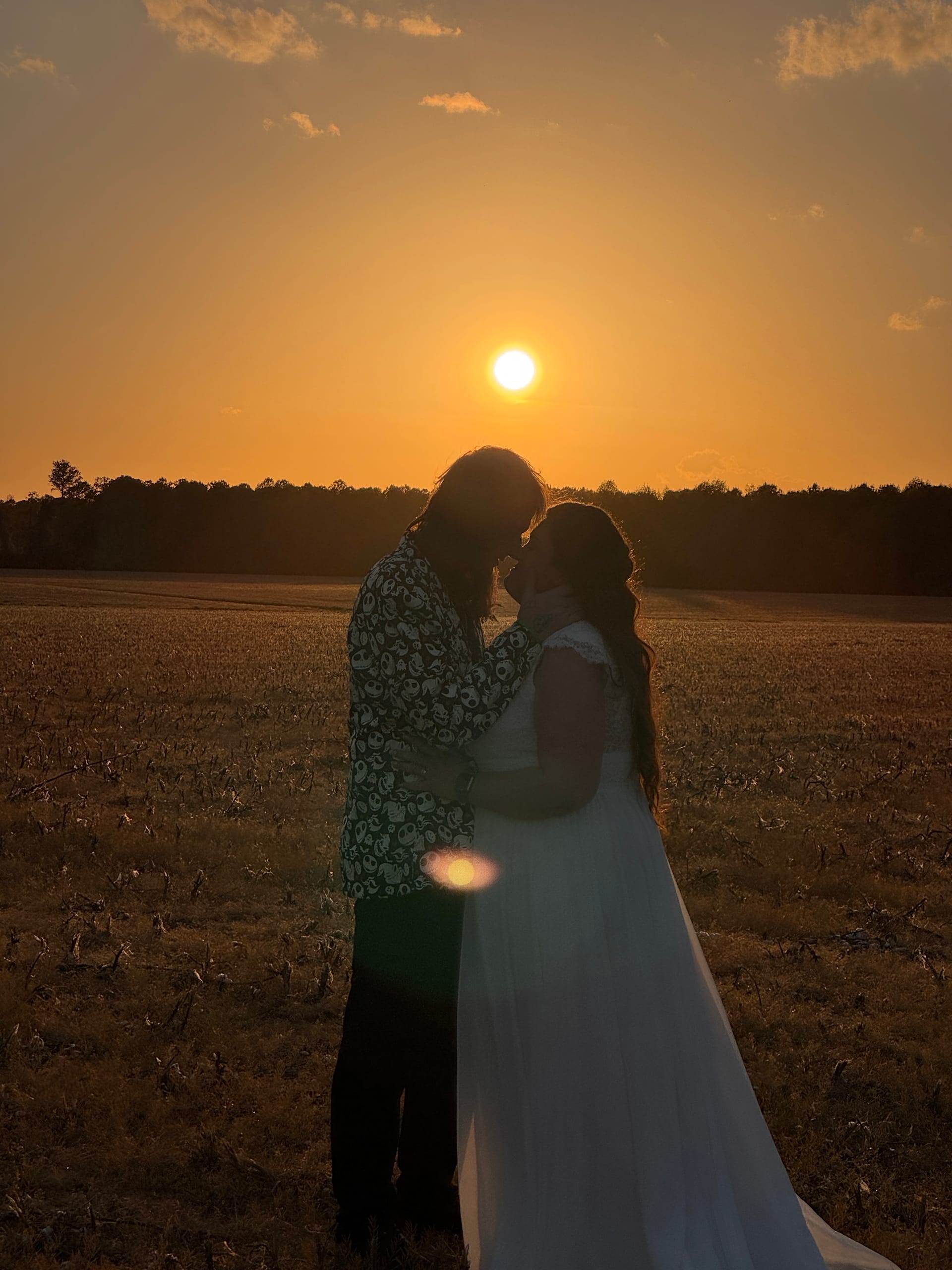 Silhouette of a bride in a flowing white gown and groom in a patterned shirt sharing an intimate forehead-touch moment in an open farmland field at golden-hour sunset at Scarborough House.