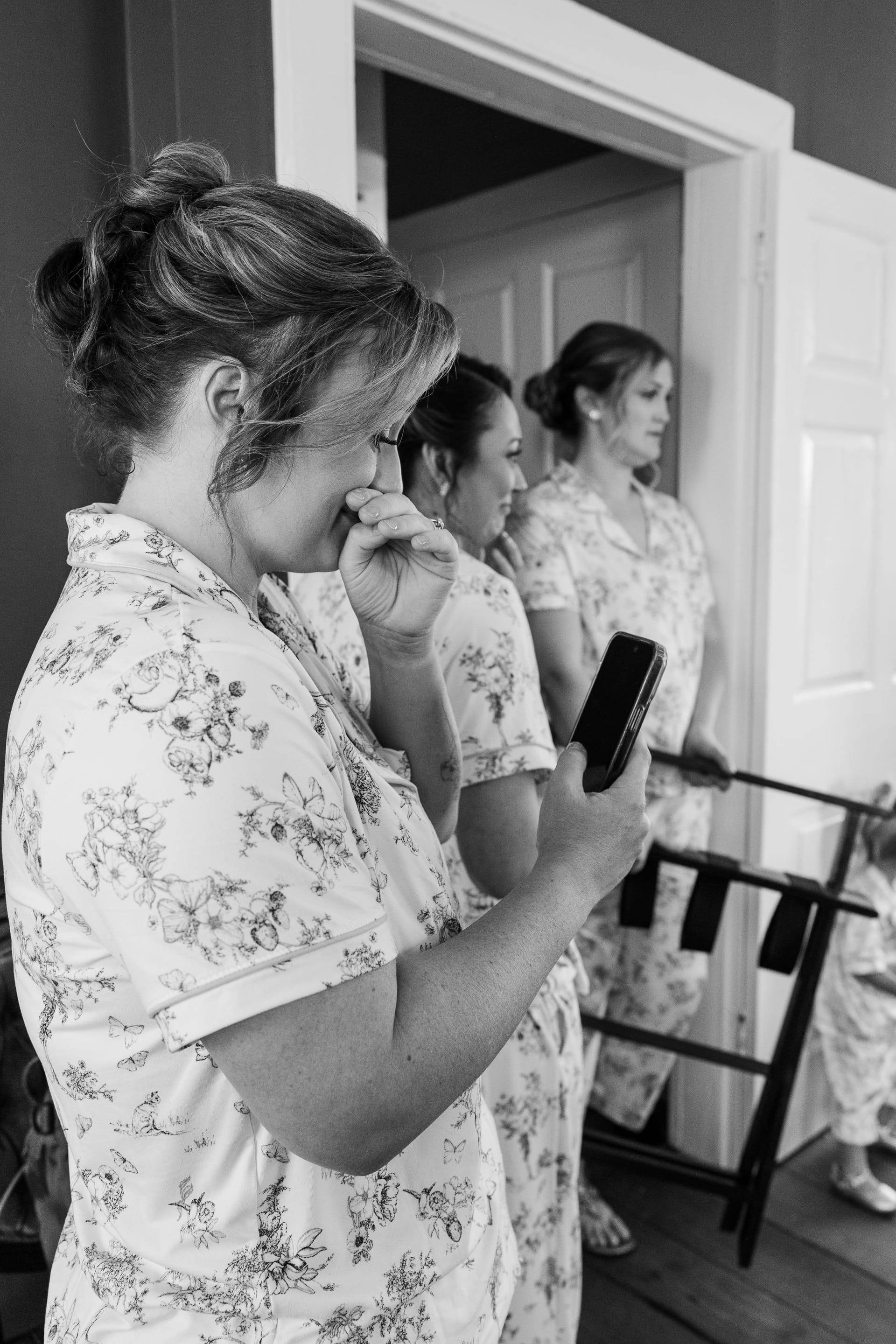 Bridesmaids in matching floral robes share an emotional moment while getting ready at Scarborough House, one wiping tears while holding her phone.