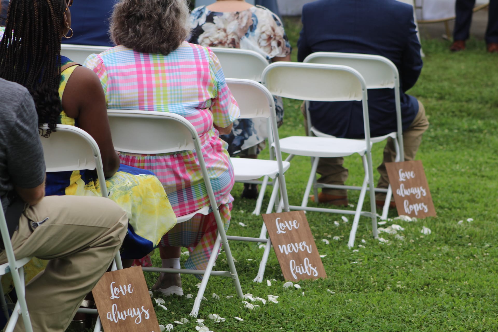 Wooden aisle signs reading Love Always, Love Never Fails, and Love Always Hopes line the white folding chairs on the outdoor ceremony lawn at Scarborough House wedding venue.