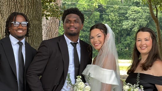 Bride in white off-shoulder gown and veil poses with three smiling guests in formal attire beneath lush oak trees at Scarborough House estate.