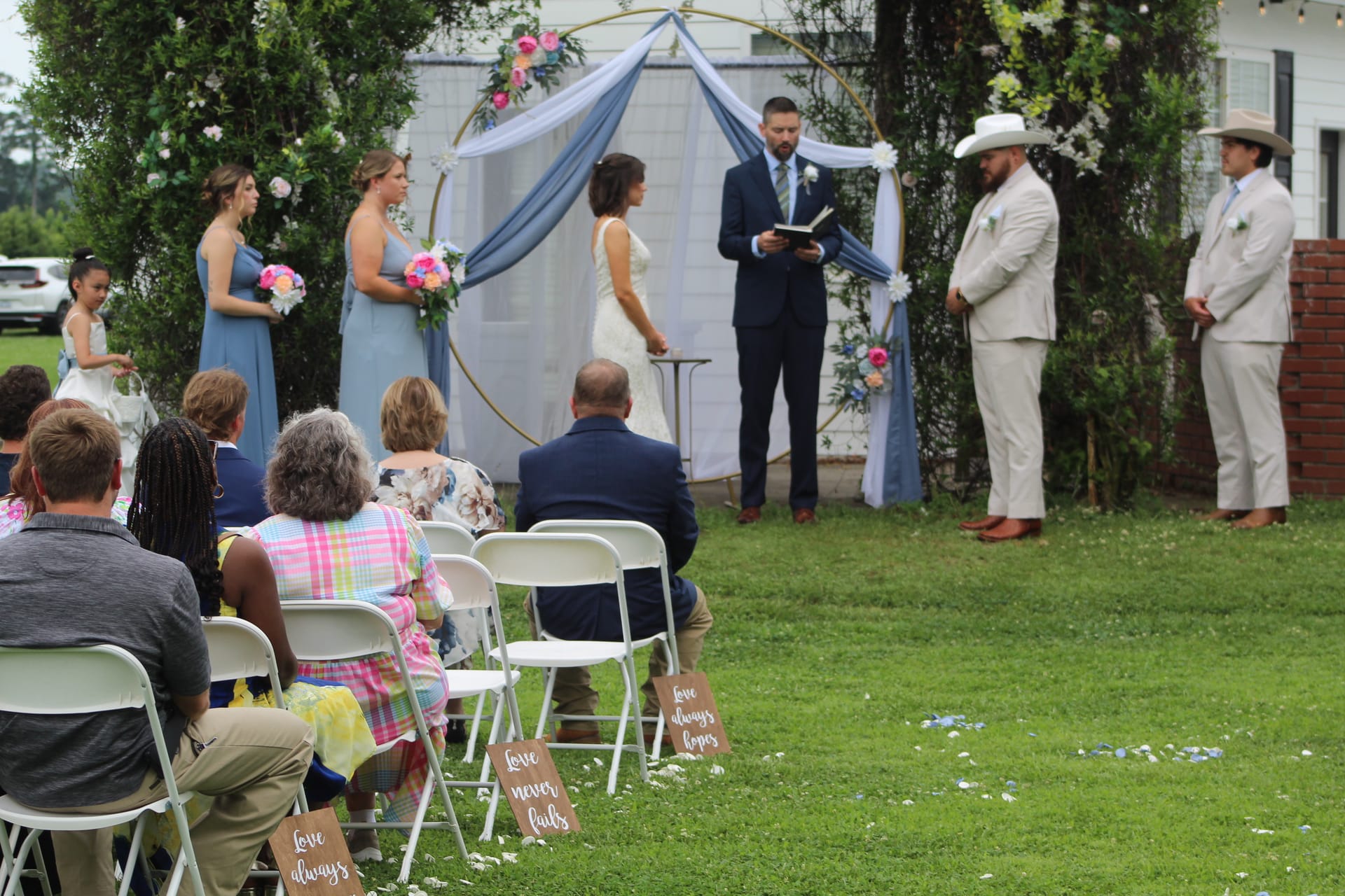 Bride and groom exchange vows beneath a gold hoop arch draped in blue fabric and colorful florals on the ceremony lawn at Scarborough House historic estate.