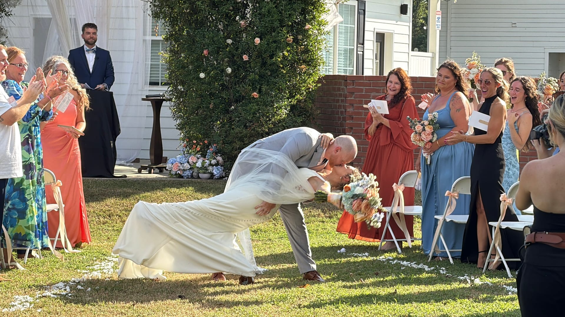 Groom dips and kisses his bride at the end of their outdoor wedding recessional on the ceremony lawn at Scarborough House as cheering guests line the aisle.