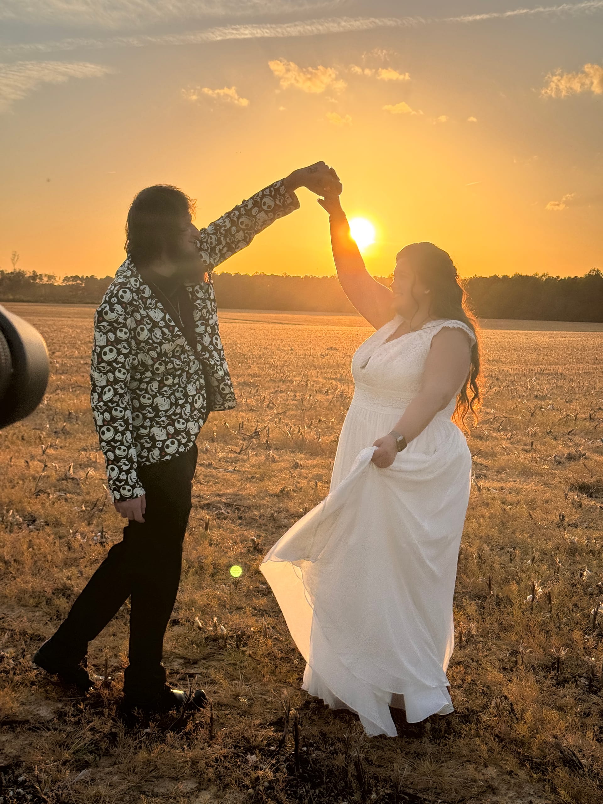Bride in a flowing white gown and groom in a patterned blazer dancing together in an open farmland field at golden-hour sunset at Scarborough House.