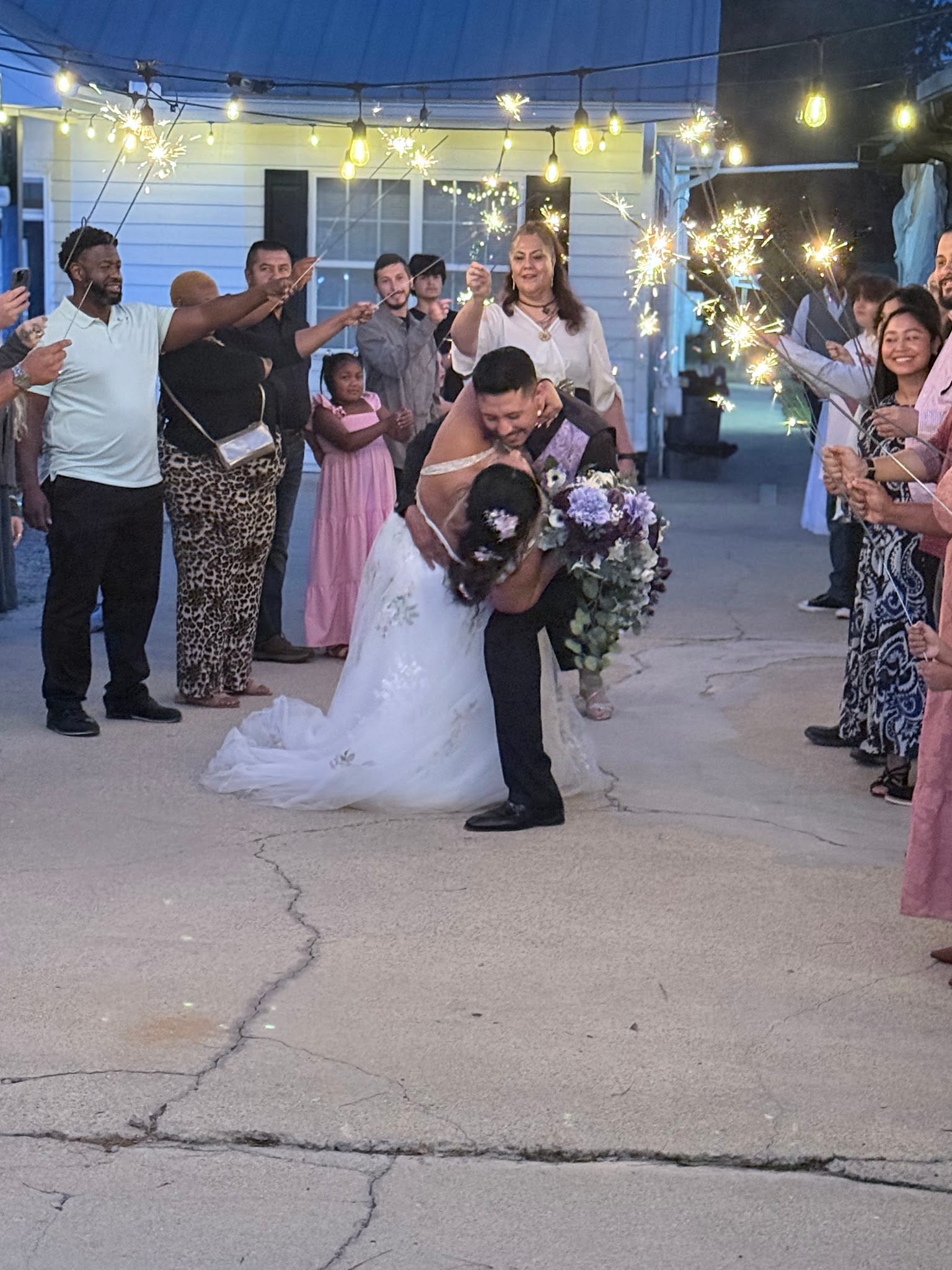 Groom dips and kisses his bride during a sparkler exit as cheering guests line the pathway under warm string lights at Scarborough House.