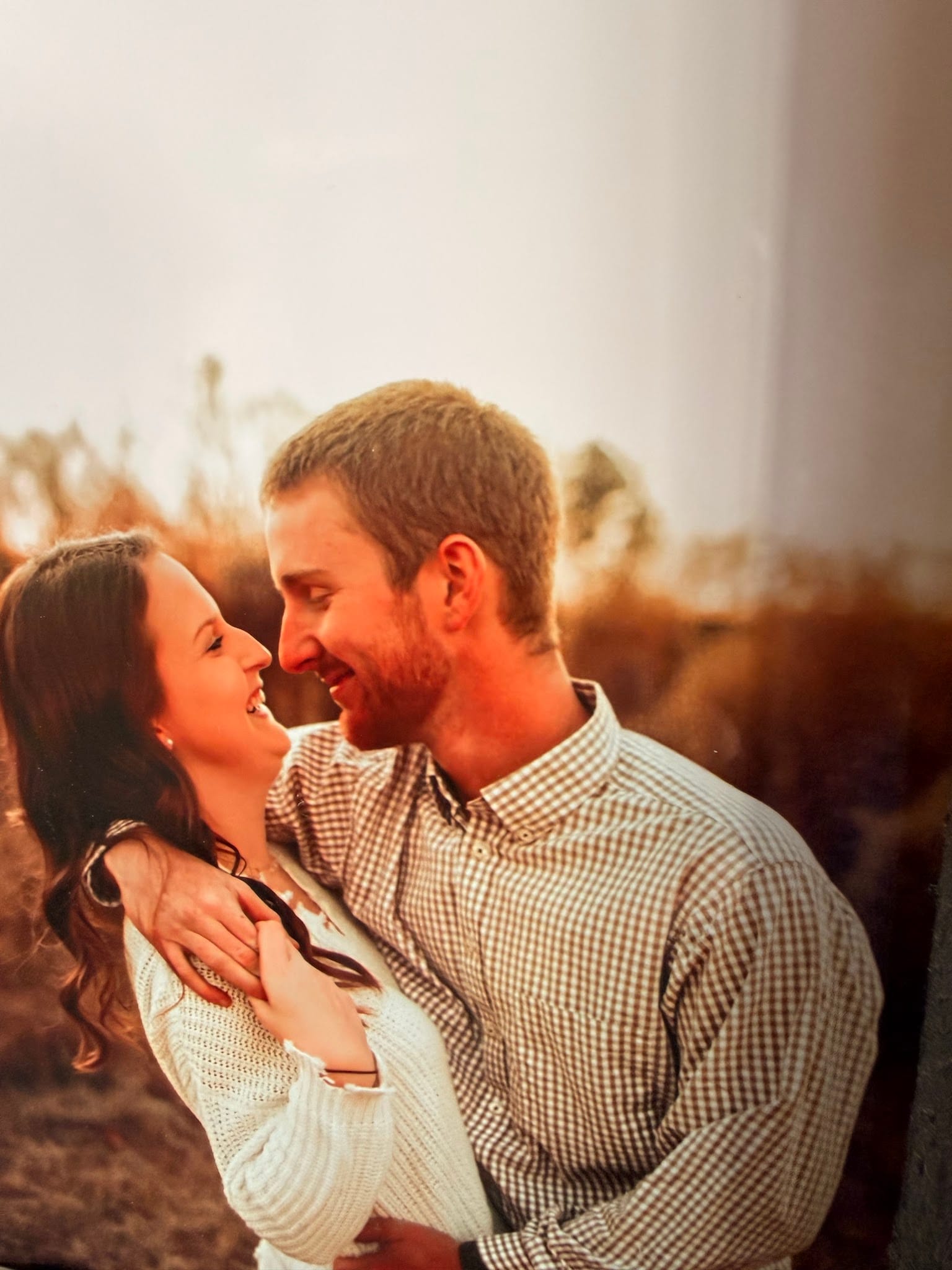 A couple smiles warmly at each other while embracing in a glowing golden-hour sunset surrounded by tall grasses at Scarborough House estate.