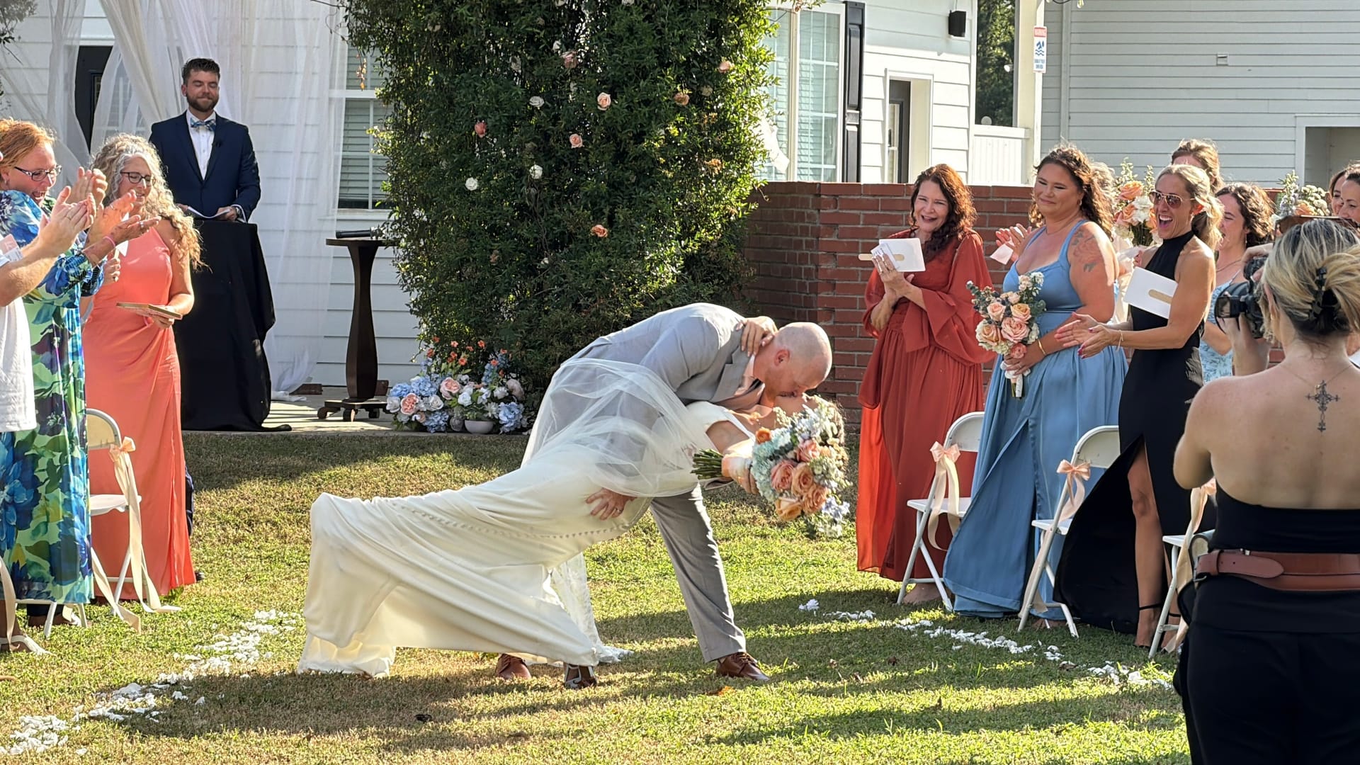 Groom dips his bride for a dramatic kiss while wedding guests cheer along the aisle of the Scarborough House ceremony lawn.