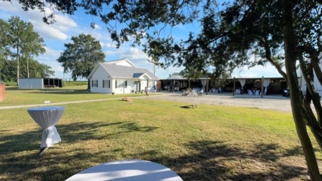Wide view of Scarborough House wedding venue showing the white historic farmhouse, draped cocktail tables on the ceremony lawn, and a tented reception pavilion surrounded by mature oak trees under a partly cloudy sky.