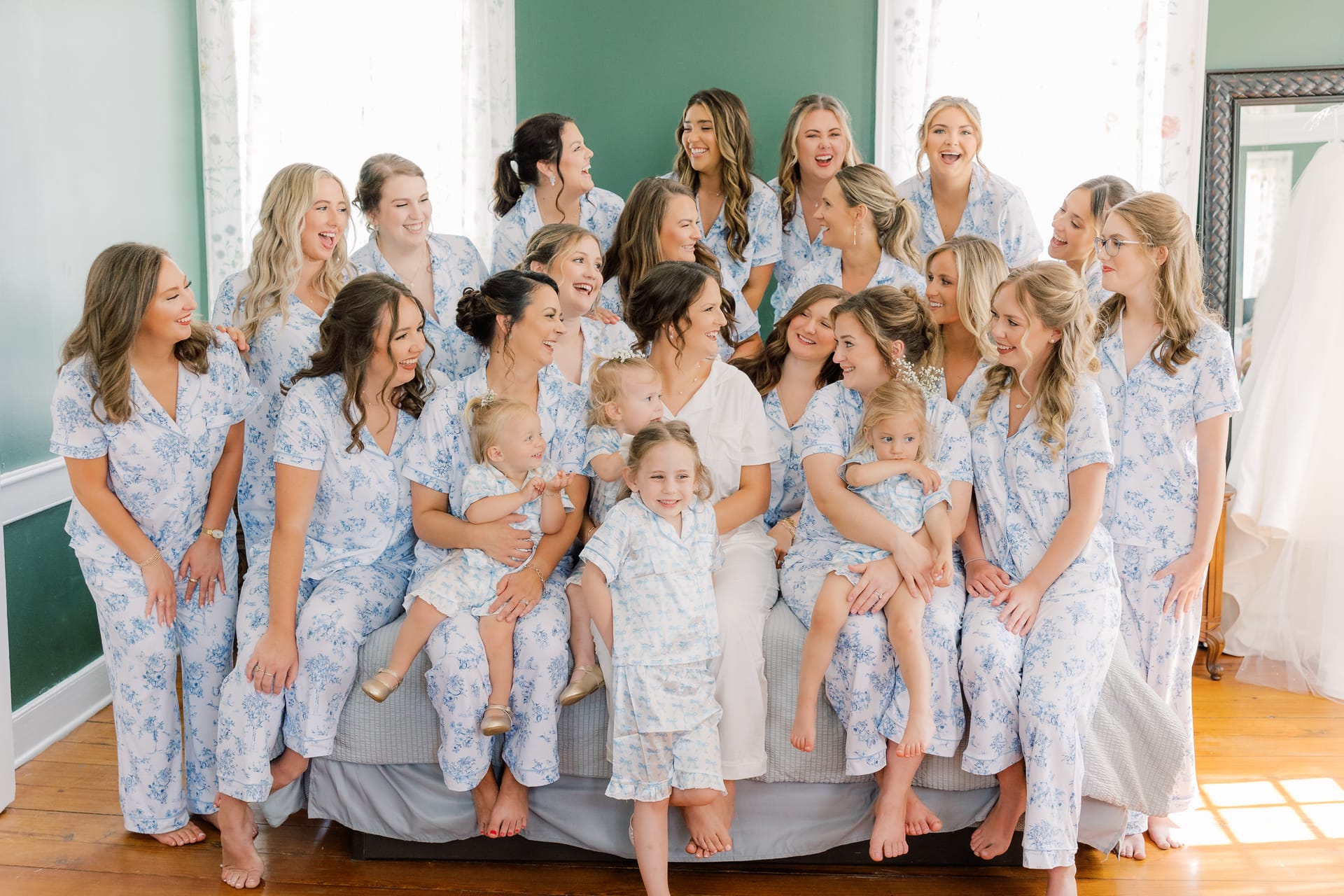 Bride in white surrounded by bridesmaids and young children all wearing matching blue floral pajamas laughing together in the bridal suite at Scarborough House.