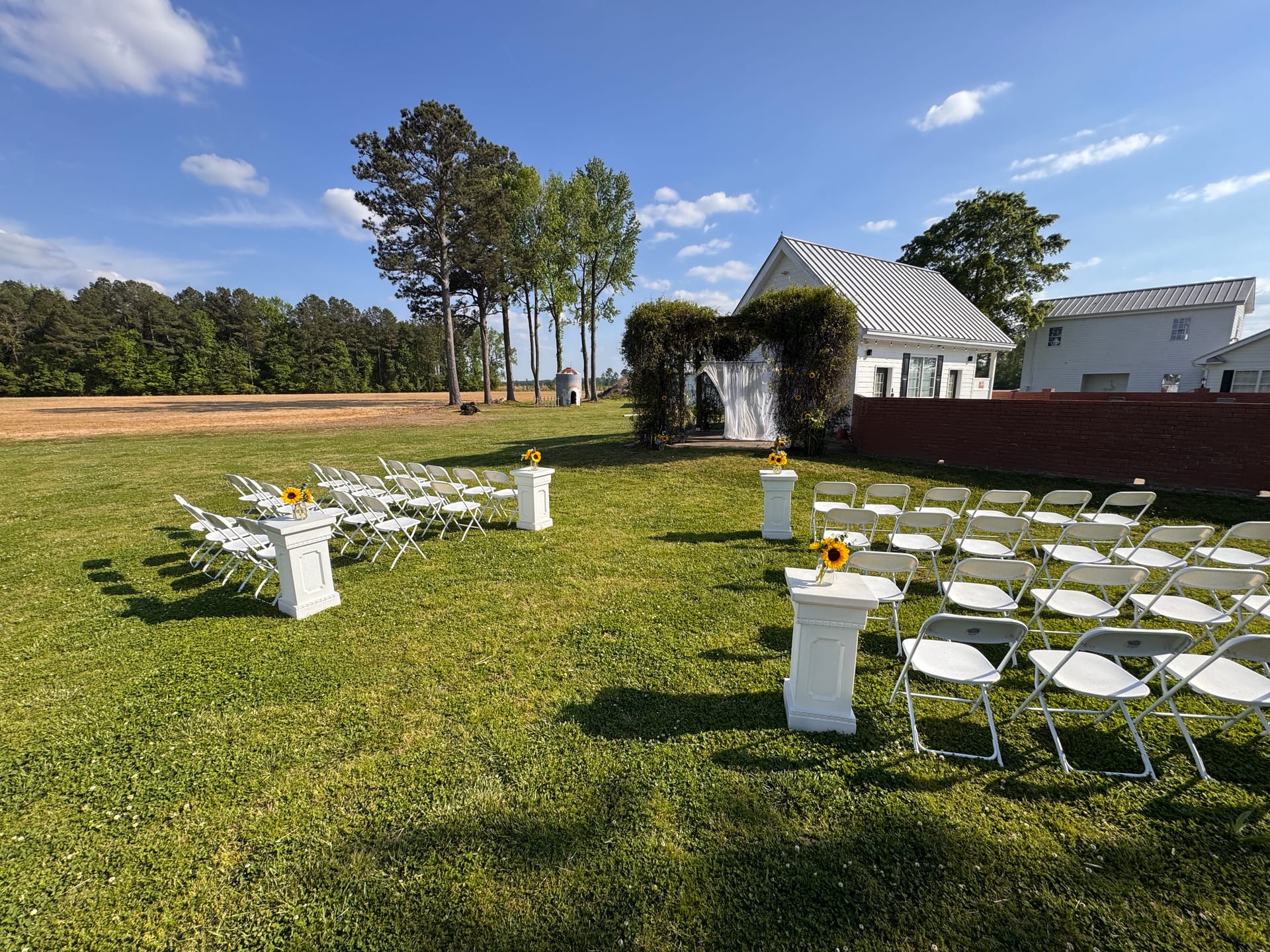 Outdoor wedding ceremony setup on the lawn at Scarborough House, with rows of white chairs, a sunflower-adorned aisle, and an ivy-covered arch.