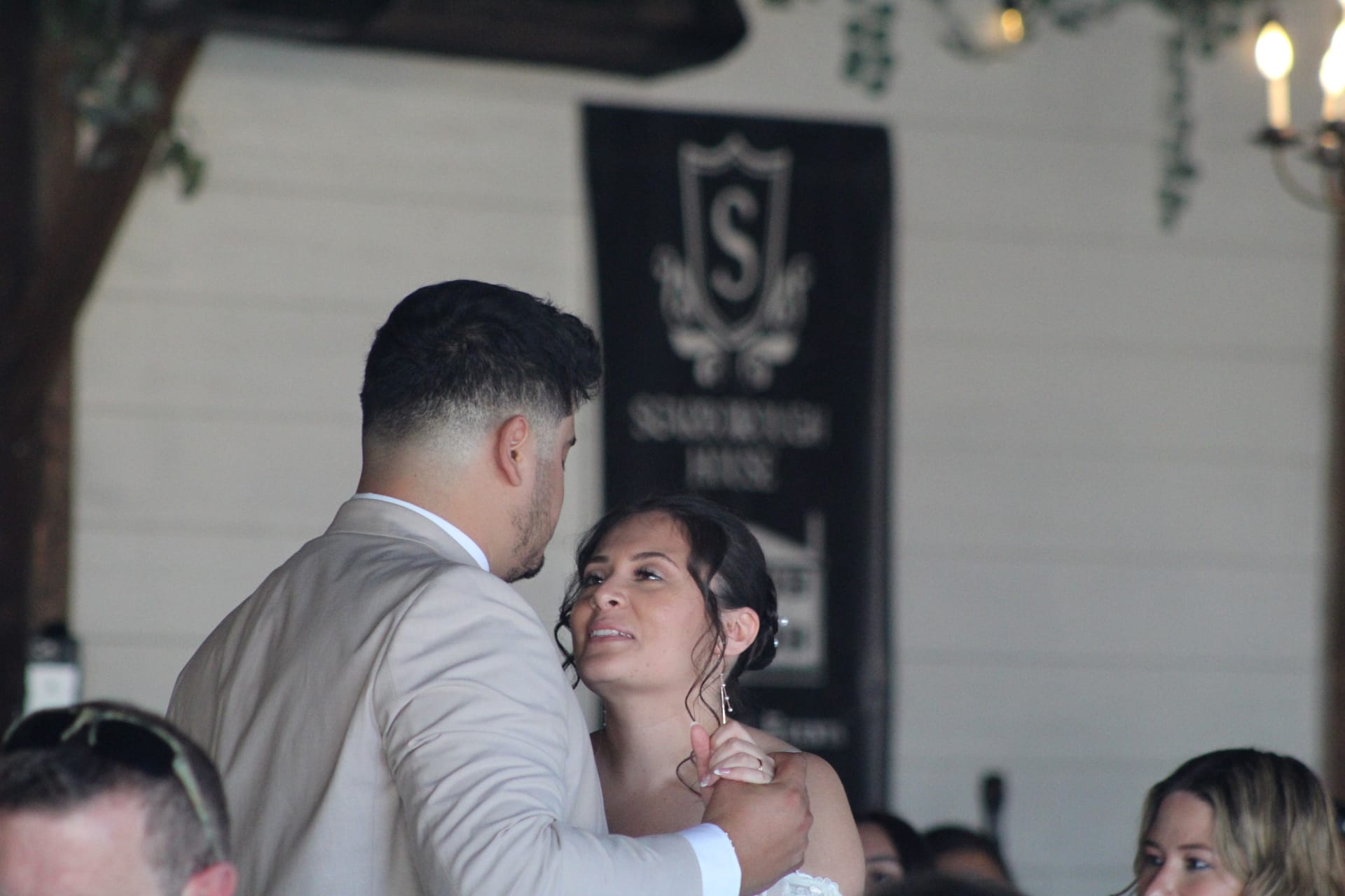 Bride gazes up tenderly at groom while sharing their first dance at Scarborough House wedding venue with the estate crest banner visible in the background.