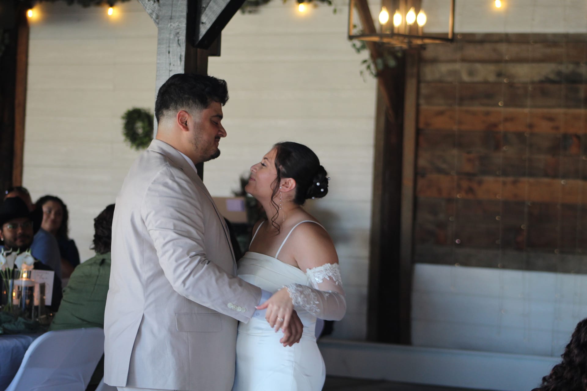 Bride in an off-shoulder white gown and groom in a beige suit share an intimate first dance inside the warmly lit grand hall at Scarborough House wedding venue.