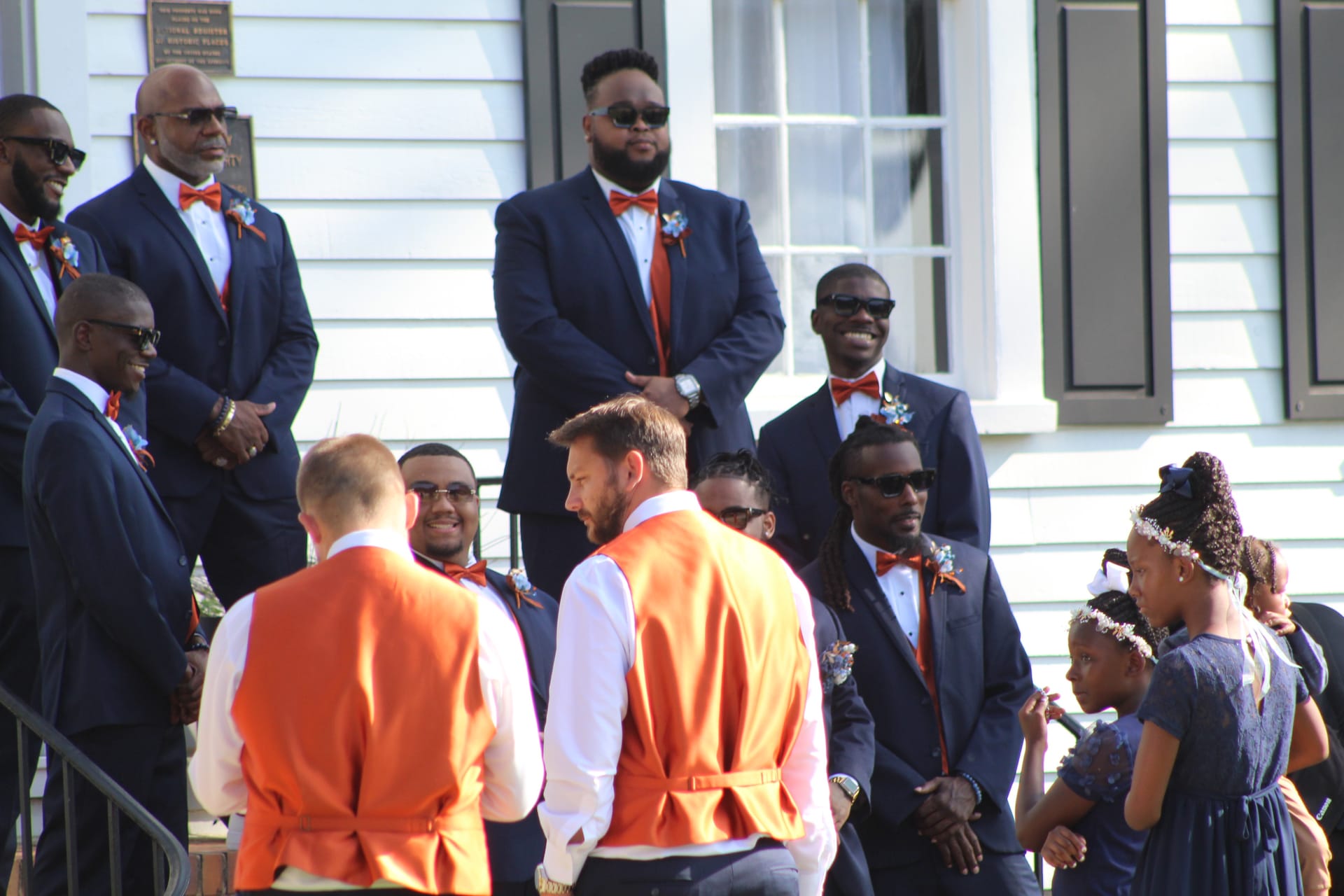 Groomsmen in navy suits with orange bow ties and boutonnières gather on the front steps of the historic 1821 Scarborough House estate before the wedding ceremony.